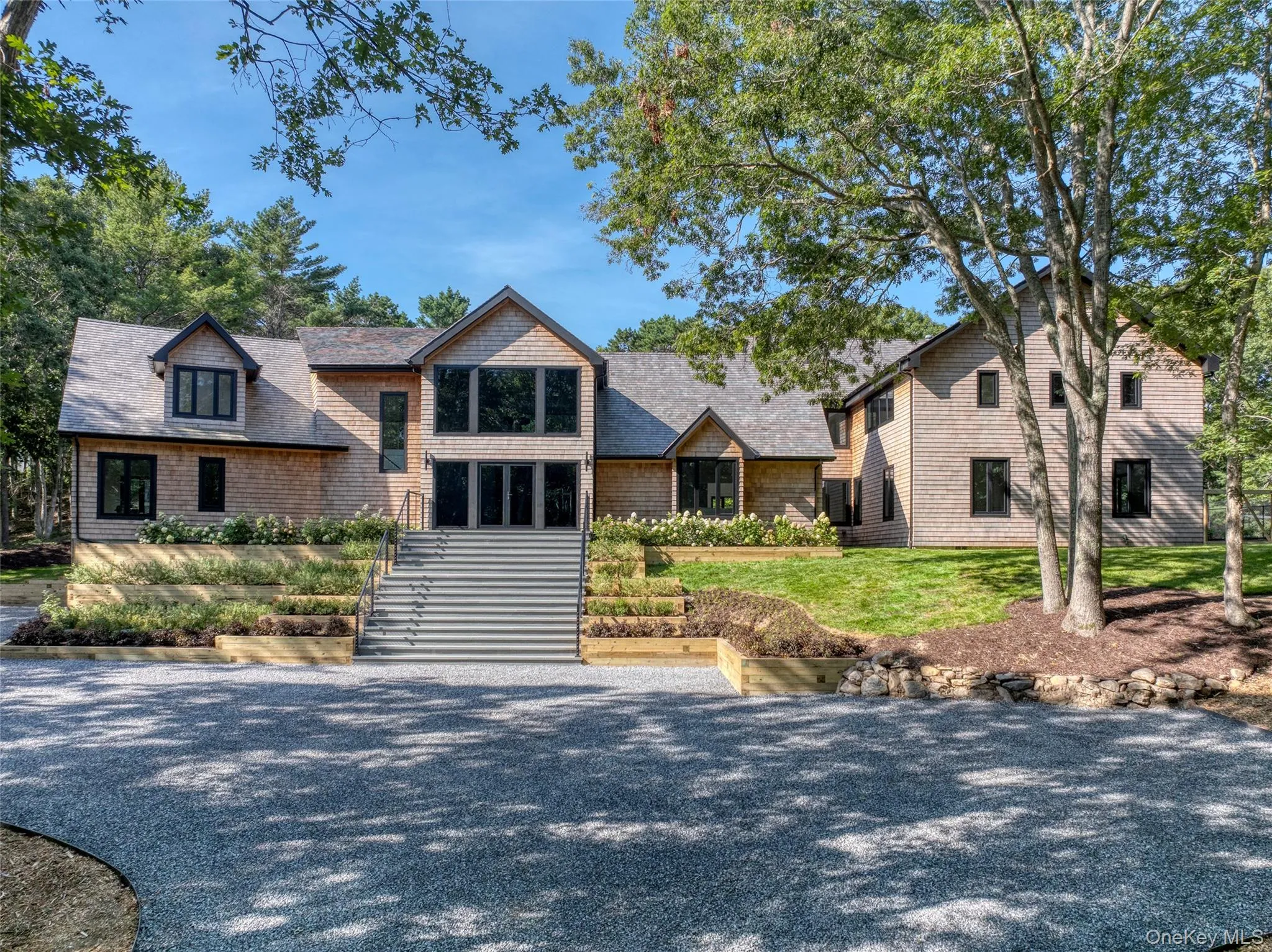 Shingle-sided exterior with a multi-gabled roof, black-framed windows, and a gravel driveway Shingle-sided exterior with a multi-gabled roof, black-framed windows, and a gravel driveway