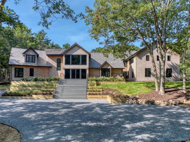 Shingle-sided exterior with a multi-gabled roof, black-framed windows, and a gravel driveway