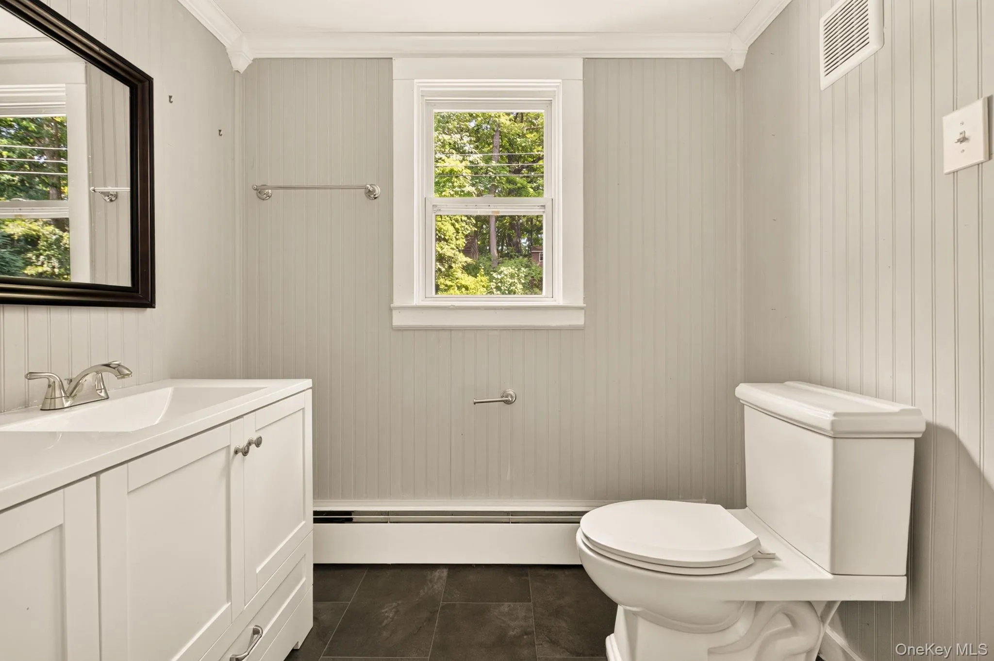 White vanity with integrated sink, chrome faucet, wall-mounted mirror, and beadboard wall paneling White vanity with integrated sink, chrome faucet, wall-mounted mirror, and beadboard wall paneling