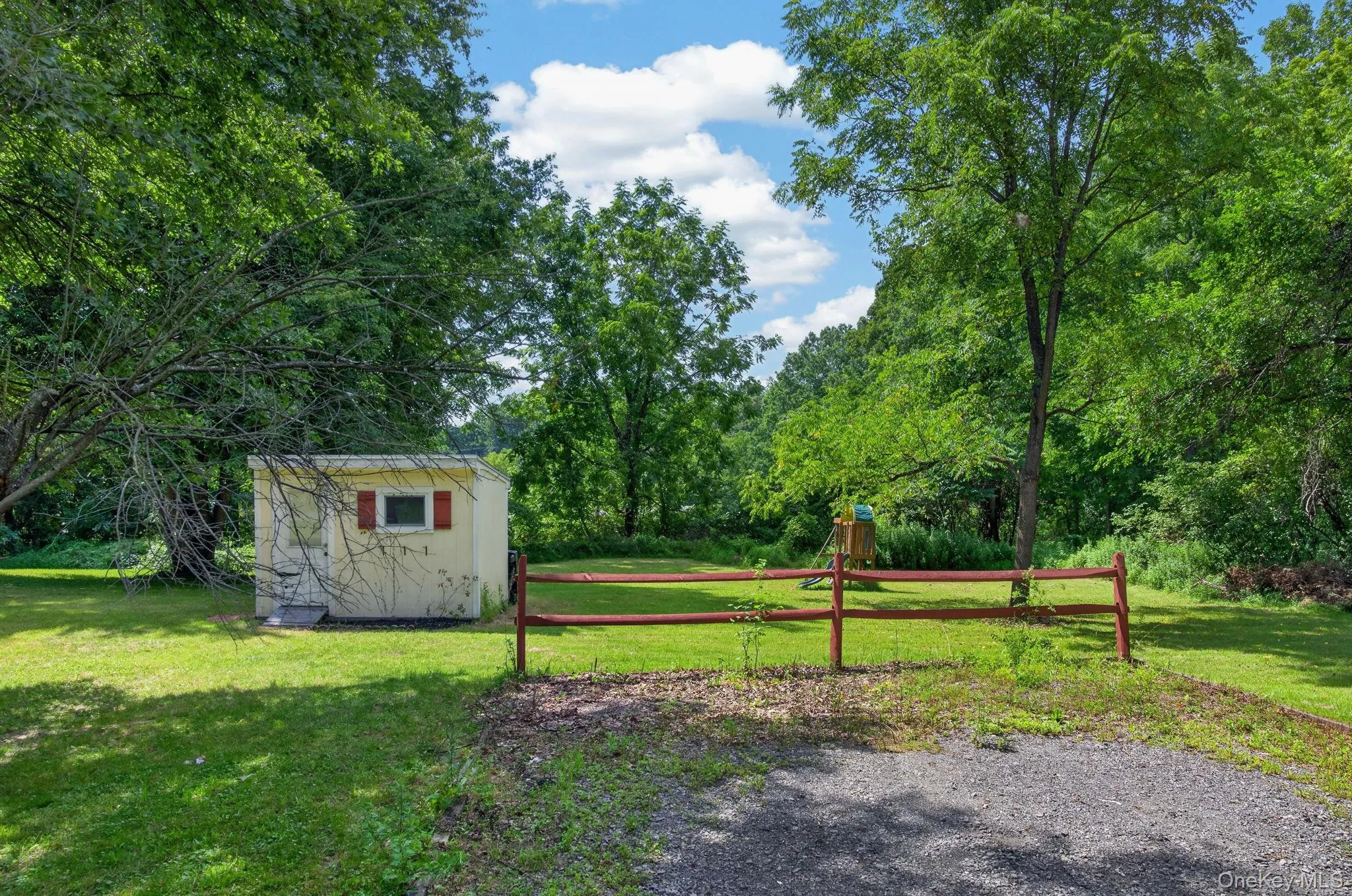 Manicured lawn with mature trees, a detached storage shed, and a rustic wood fence Manicured lawn with mature trees, a detached storage shed, and a rustic wood fence