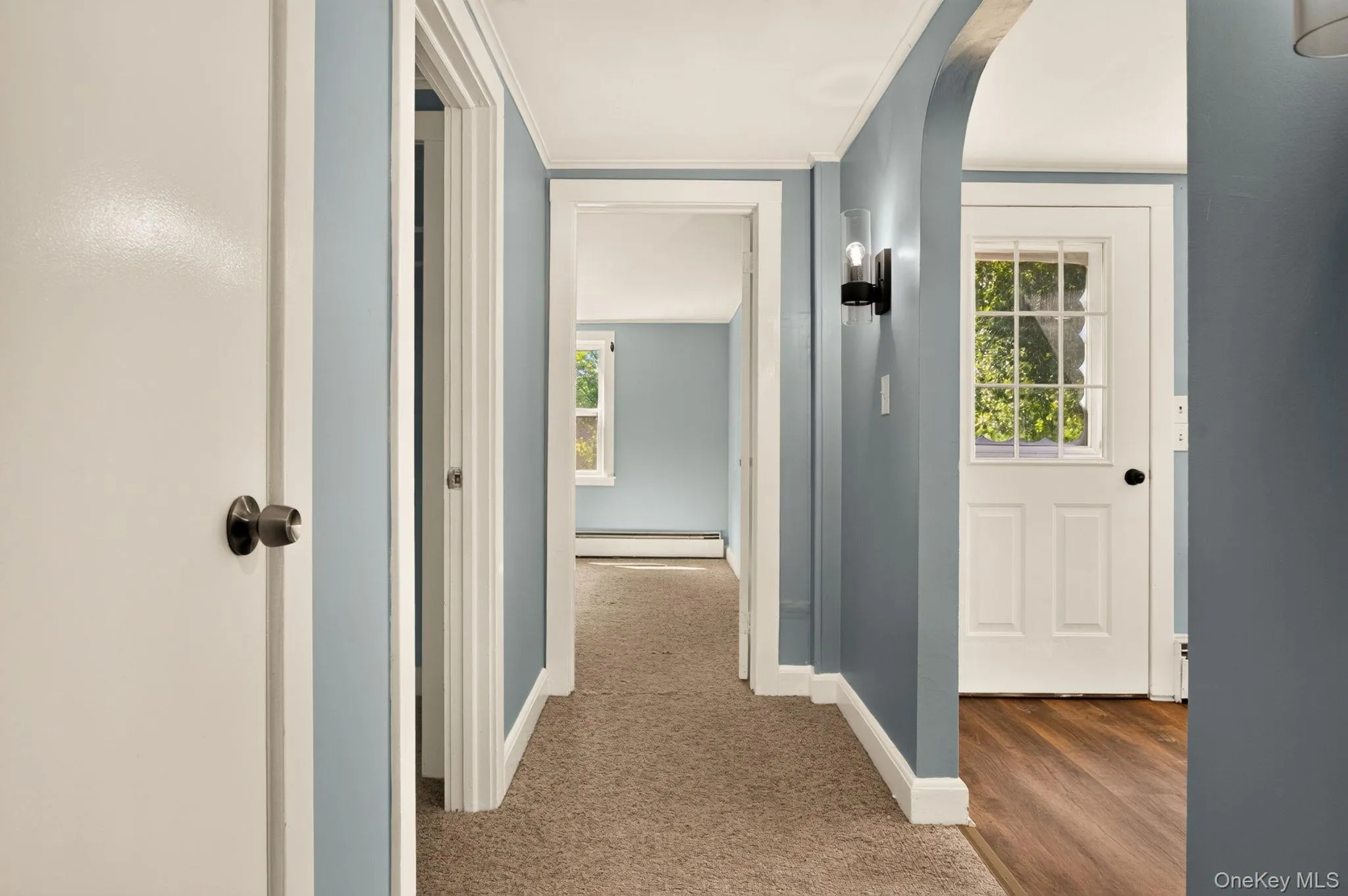 Hallway featuring painted walls, white trim, and a combination of carpet and wood-finish flooring Hallway featuring painted walls, white trim, and a combination of carpet and wood-finish flooring
