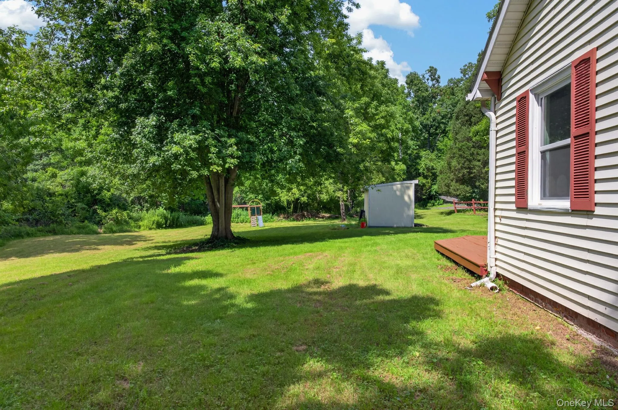 Expansive green lawn with mature shade tree, a separate storage shed, and a side deck Expansive green lawn with mature shade tree, a separate storage shed, and a side deck