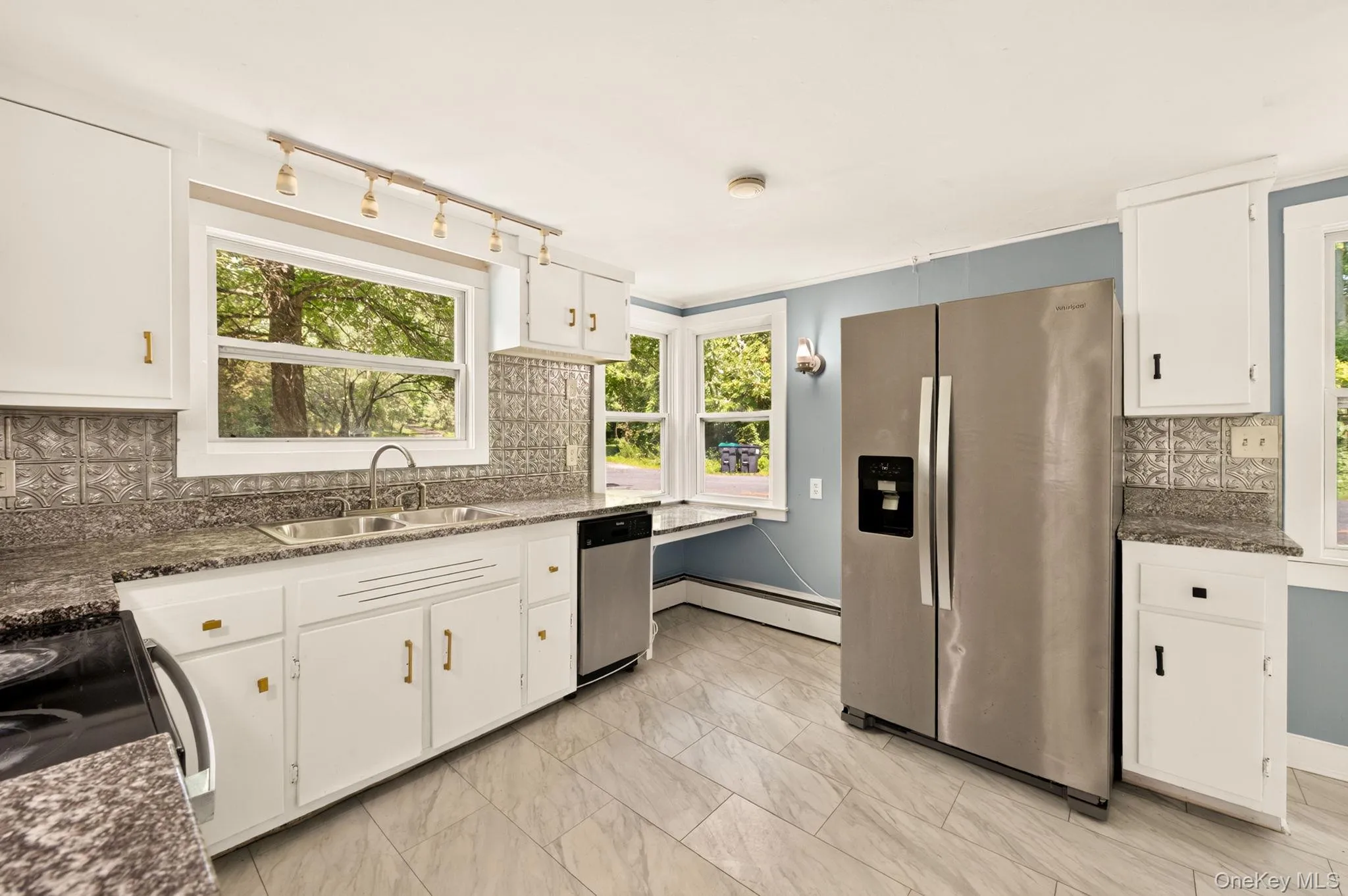 White cabinetry, stainless steel appliances, textured backsplash, stone-finish countertops, and tile flooring White cabinetry, stainless steel appliances, textured backsplash, stone-finish countertops, and tile flooring
