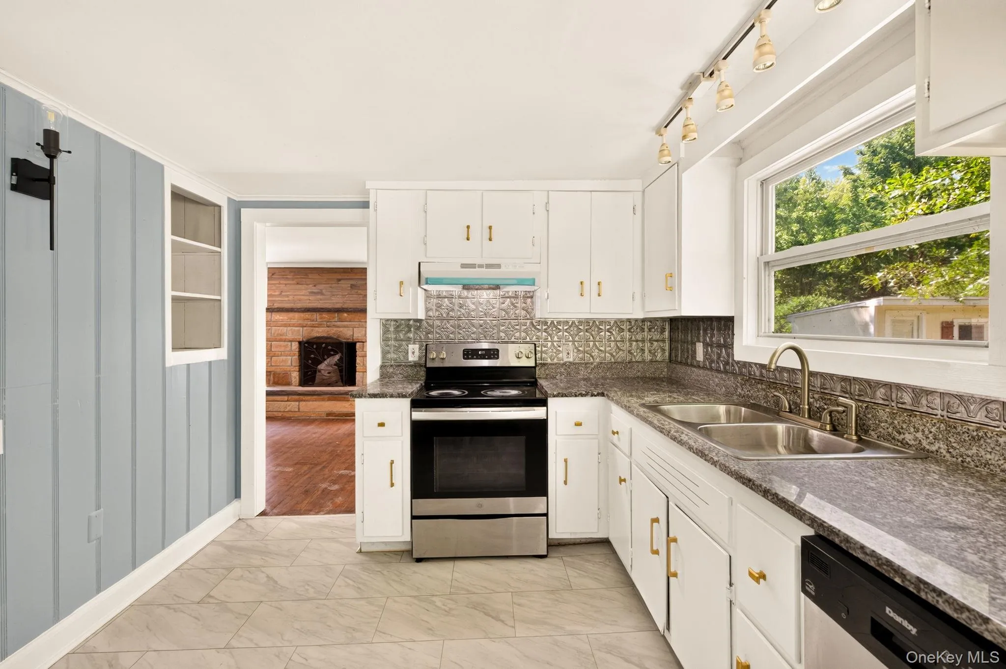 Bright, updated kitchen featuring white cabinetry with brass hardware, stainless steel gas range, dual basin sink with brushed nickel faucet, and gray quartz countertops Bright, updated kitchen featuring white cabinetry with brass hardware, stainless steel gas range, dual basin sink with brushed nickel faucet, and gray quartz countertops