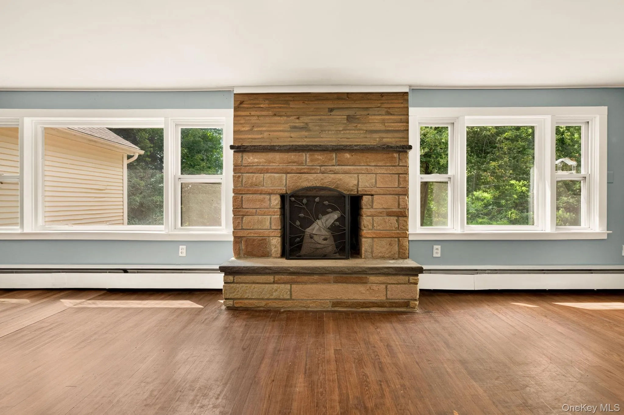 Stone-clad fireplace with a hearth, wood-finish flooring, and multiple windows Stone-clad fireplace with a hearth, wood-finish flooring, and multiple windows