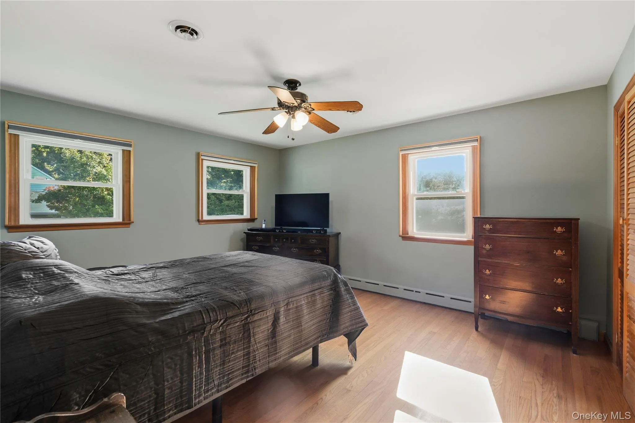 Wood-finish flooring, two windows with wood trim, ceiling fan, and a built-in closet with louvered doors Wood-finish flooring, two windows with wood trim, ceiling fan, and a built-in closet with louvered doors