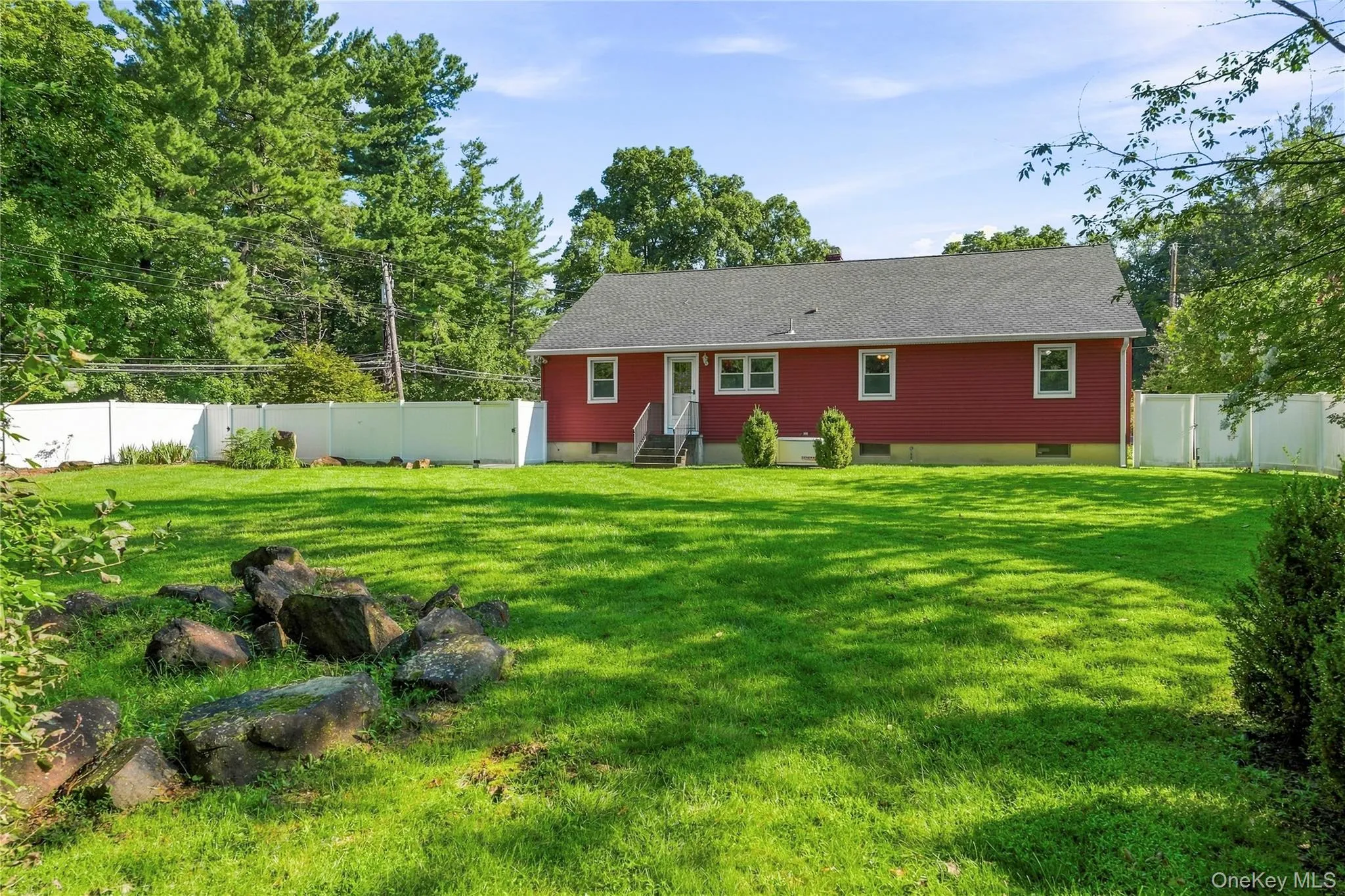 Expansive green lawn, white privacy fencing, red exterior siding, mature trees, and a ground-level rock feature Expansive green lawn, white privacy fencing, red exterior siding, mature trees, and a ground-level rock feature