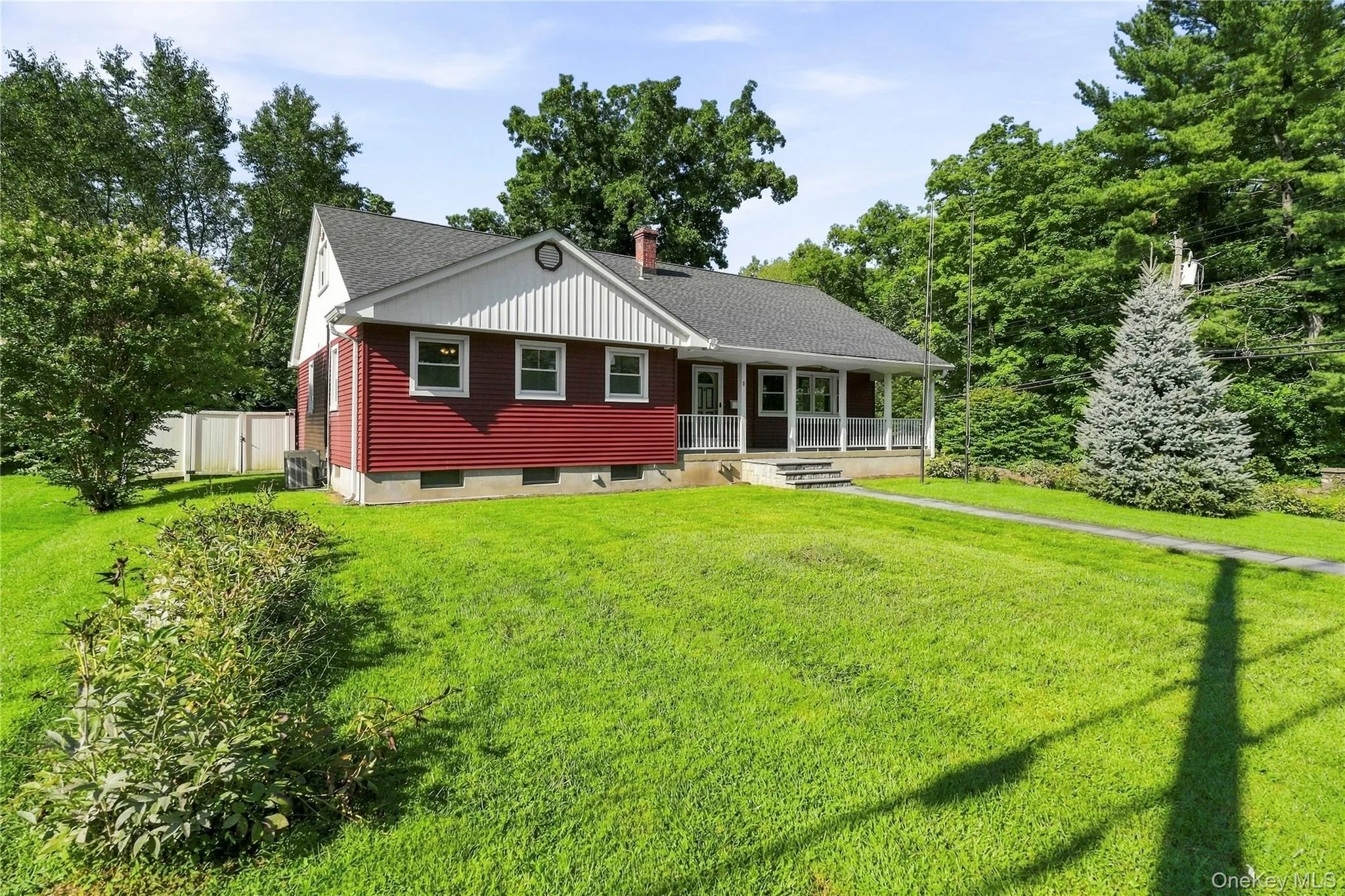 Red exterior siding with white trim, covered front porch, dark shingled roof, mature landscaping, and an expansive lawn Red exterior siding with white trim, covered front porch, dark shingled roof, mature landscaping, and an expansive lawn