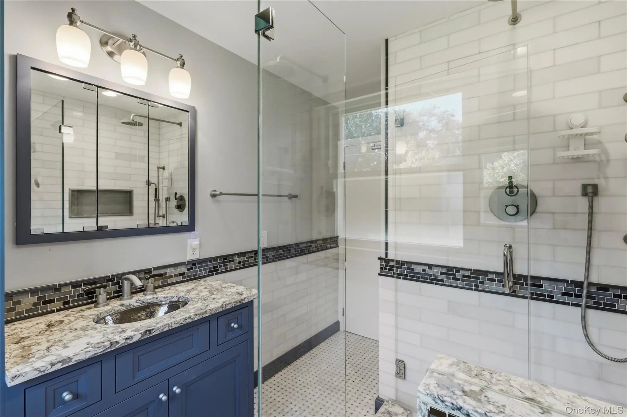 Vanity with stone countertop and undermount sink, walk-in shower with glass enclosure, subway tile shower surround, and mosaic tile accents Vanity with stone countertop and undermount sink, walk-in shower with glass enclosure, subway tile shower surround, and mosaic tile accents
