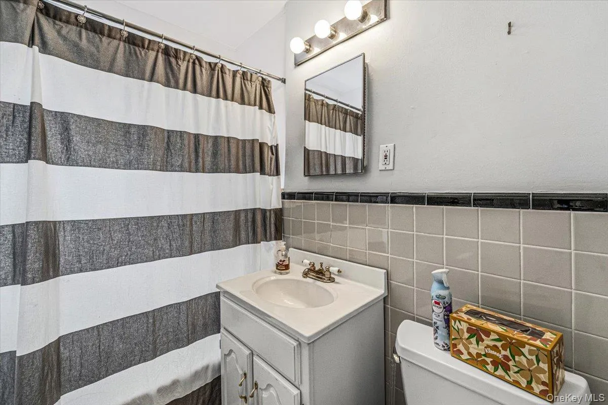 Bathroom featuring a vanity with an integrated sink, wall-mounted mirror, overhead lighting fixture, and tiled walls Bathroom featuring a vanity with an integrated sink, wall-mounted mirror, overhead lighting fixture, and tiled walls