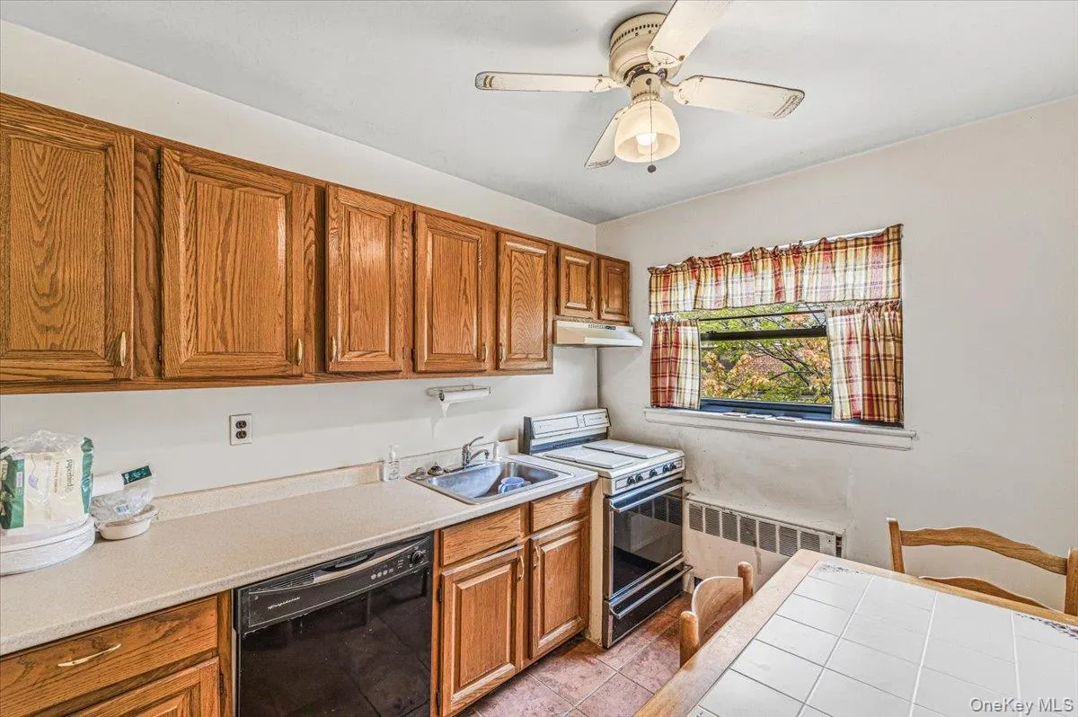 Kitchen featuring wood cabinetry, stainless steel sink, black dishwasher, and a ceiling fan with integrated lighting Kitchen featuring wood cabinetry, stainless steel sink, black dishwasher, and a ceiling fan with integrated lighting
