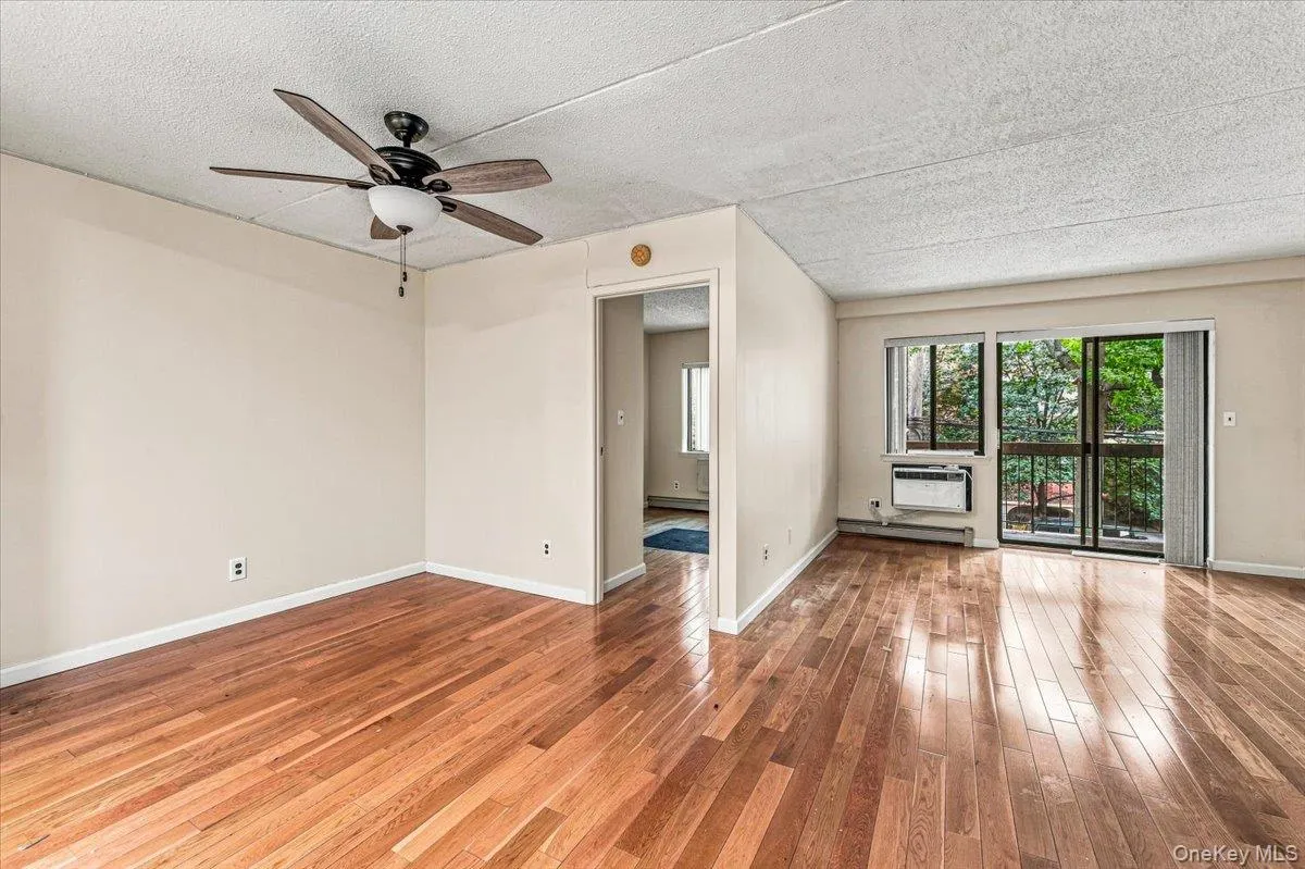 Hardwood flooring, ceiling fan with integrated lighting, sliding glass door, and wall-mounted air conditioning unit Hardwood flooring, ceiling fan with integrated lighting, sliding glass door, and wall-mounted air conditioning unit