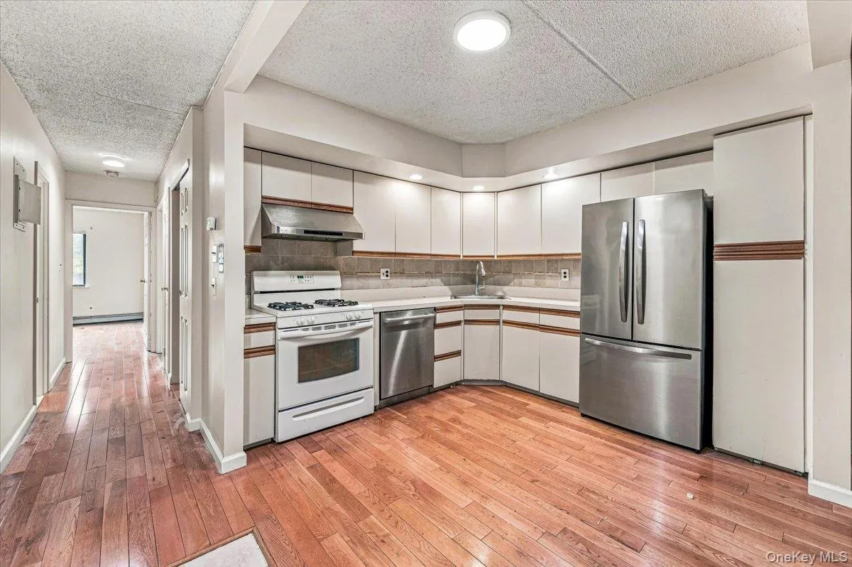 Kitchen featuring wood-finish flooring, white cabinetry, integrated stainless steel appliances, and a tiled backsplash Kitchen featuring wood-finish flooring, white cabinetry, integrated stainless steel appliances, and a tiled backsplash