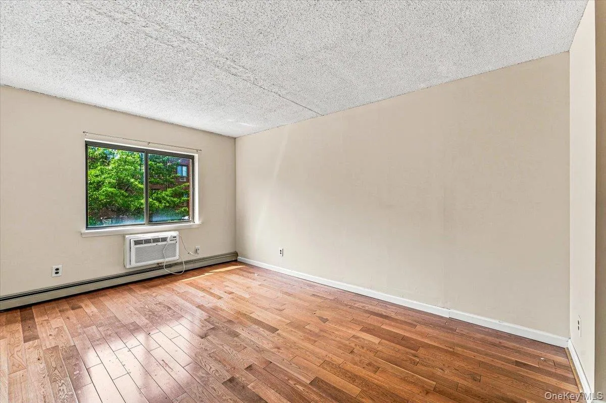 Hardwood flooring, neutral wall tones, window-mounted air conditioning unit, and a window providing exterior views Hardwood flooring, neutral wall tones, window-mounted air conditioning unit, and a window providing exterior views