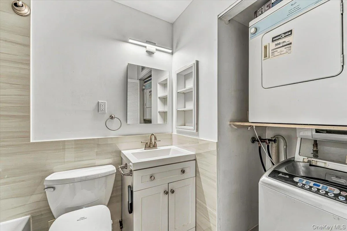 White vanity with integrated sink, chrome faucet, wall-mounted medicine cabinet, and stacked laundry appliances White vanity with integrated sink, chrome faucet, wall-mounted medicine cabinet, and stacked laundry appliances
