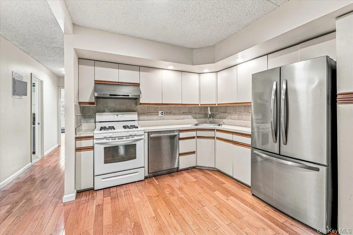 Kitchen with white cabinetry, stainless steel refrigerator, stainless steel dishwasher, white range with overhead exhaust, and wood-finish flooring Kitchen with white cabinetry, stainless steel refrigerator, stainless steel dishwasher, white range with overhead exhaust, and wood-finish flooring