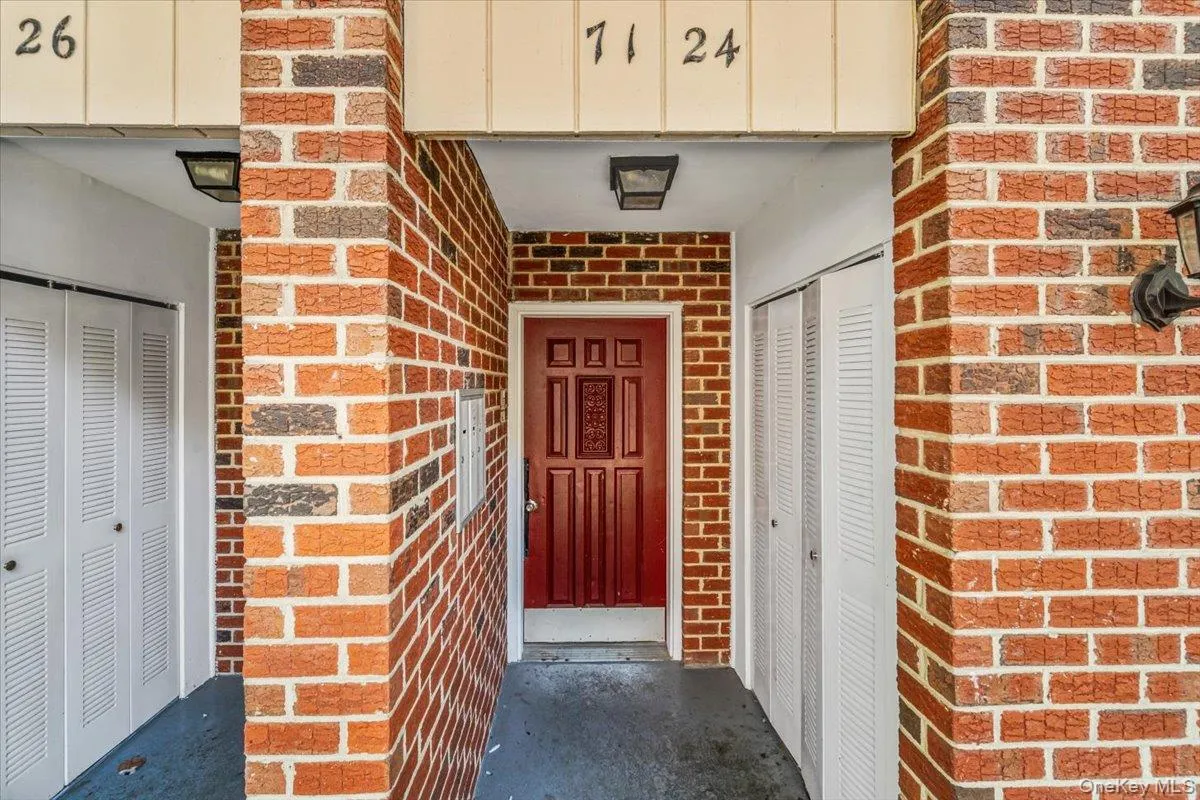 Brick exterior facade with a paneled red entry door, two louvered bifold closet doors, and outdoor sconce lighting Brick exterior facade with a paneled red entry door, two louvered bifold closet doors, and outdoor sconce lighting