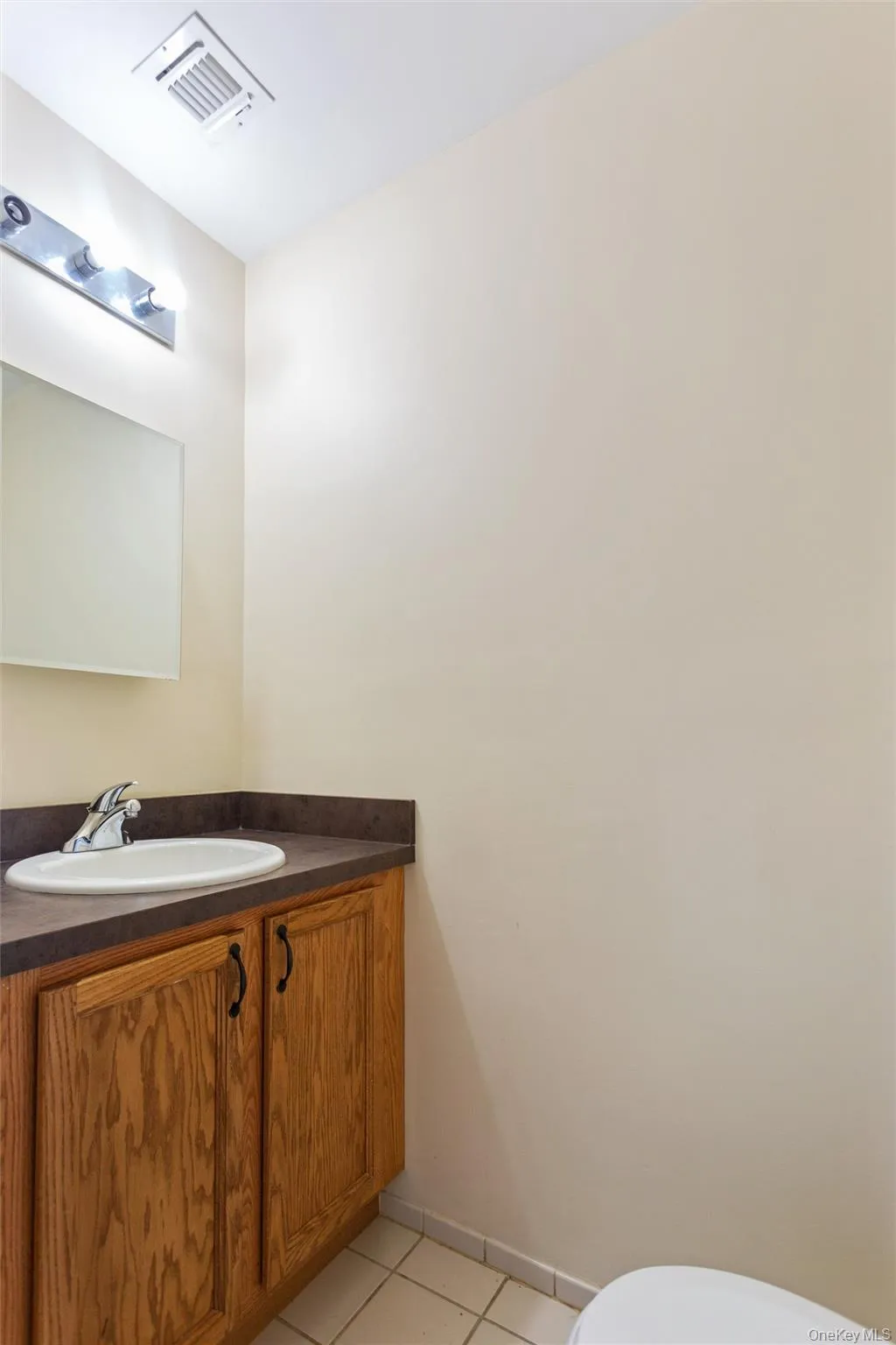 Compact powder room featuring a wood-finish vanity with dual cabinet doors, dark countertop surface, and round undermount sink Compact powder room featuring a wood-finish vanity with dual cabinet doors, dark countertop surface, and round undermount sink