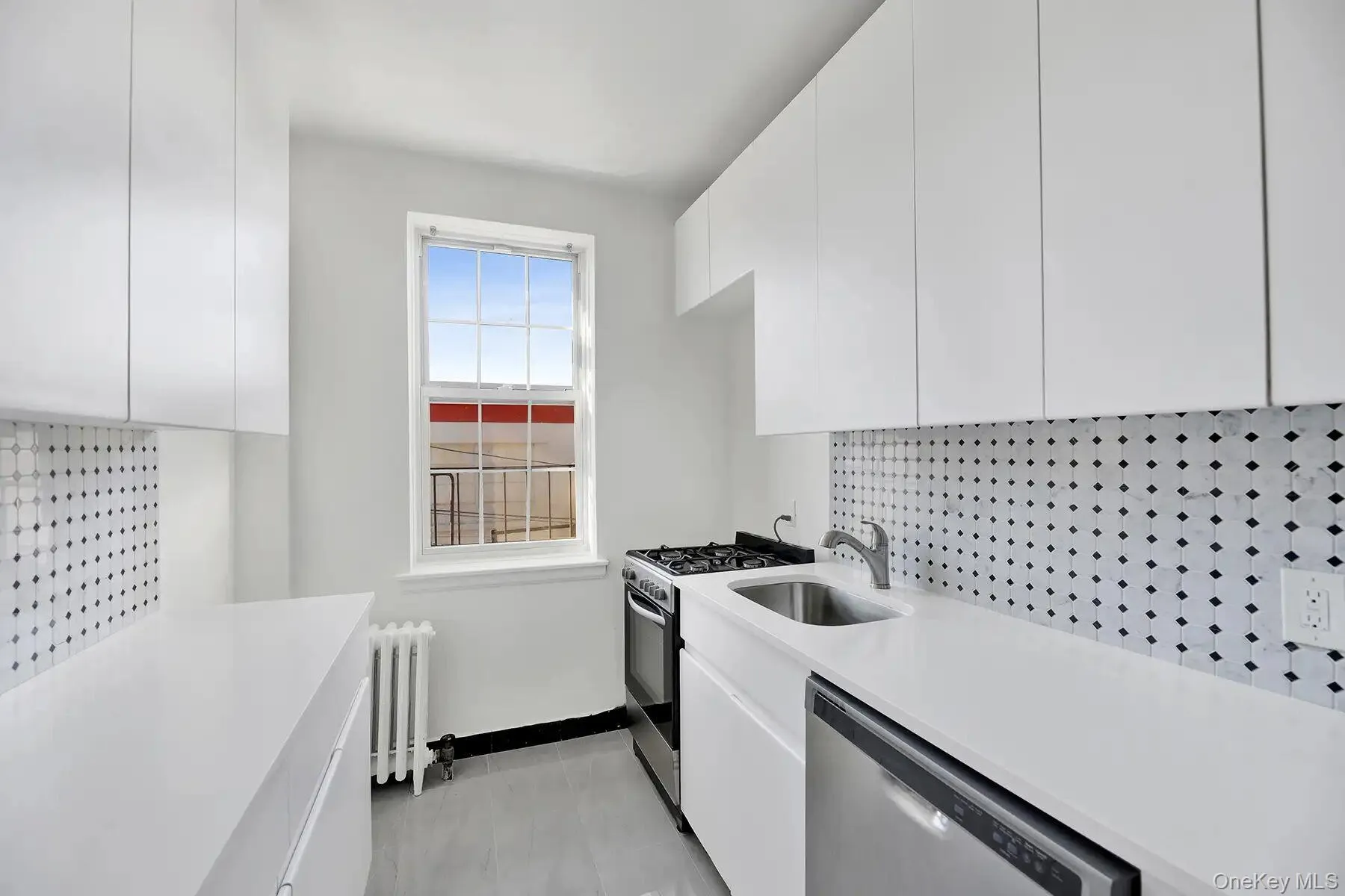 White cabinetry, white countertops, tile backsplash with black accents, stainless steel sink, and a window with security bars White cabinetry, white countertops, tile backsplash with black accents, stainless steel sink, and a window with security bars