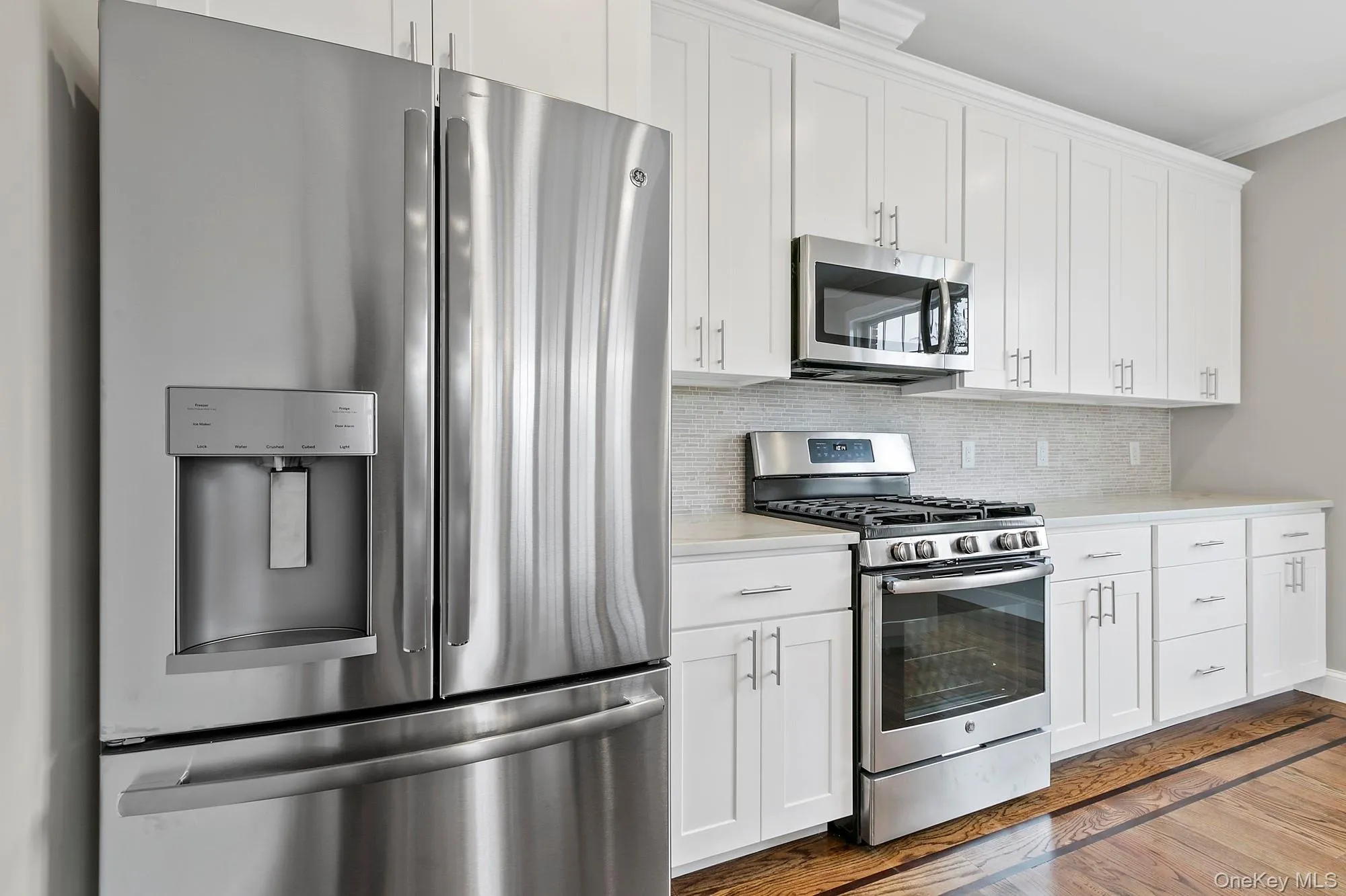 Kitchen with light hardwood / wood-style flooring, backsplash, white cabinetry, appliances with stainless steel finishes, and crown molding Kitchen with light hardwood / wood-style flooring, backsplash, white cabinetry, appliances with stainless steel finishes, and crown molding