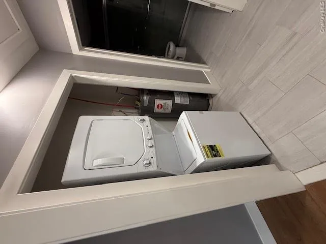 Laundry area with light wood-style floors, stacked washer and clothes dryer, and water heater Laundry area with light wood-style floors, stacked washer and clothes dryer, and water heater