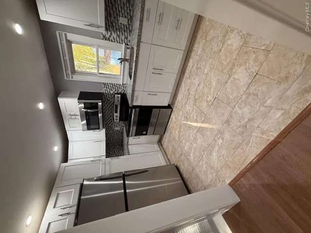 Kitchen with stainless steel appliances, white cabinetry, light stone countertops, backsplash, and recessed lighting Kitchen with stainless steel appliances, white cabinetry, light stone countertops, backsplash, and recessed lighting