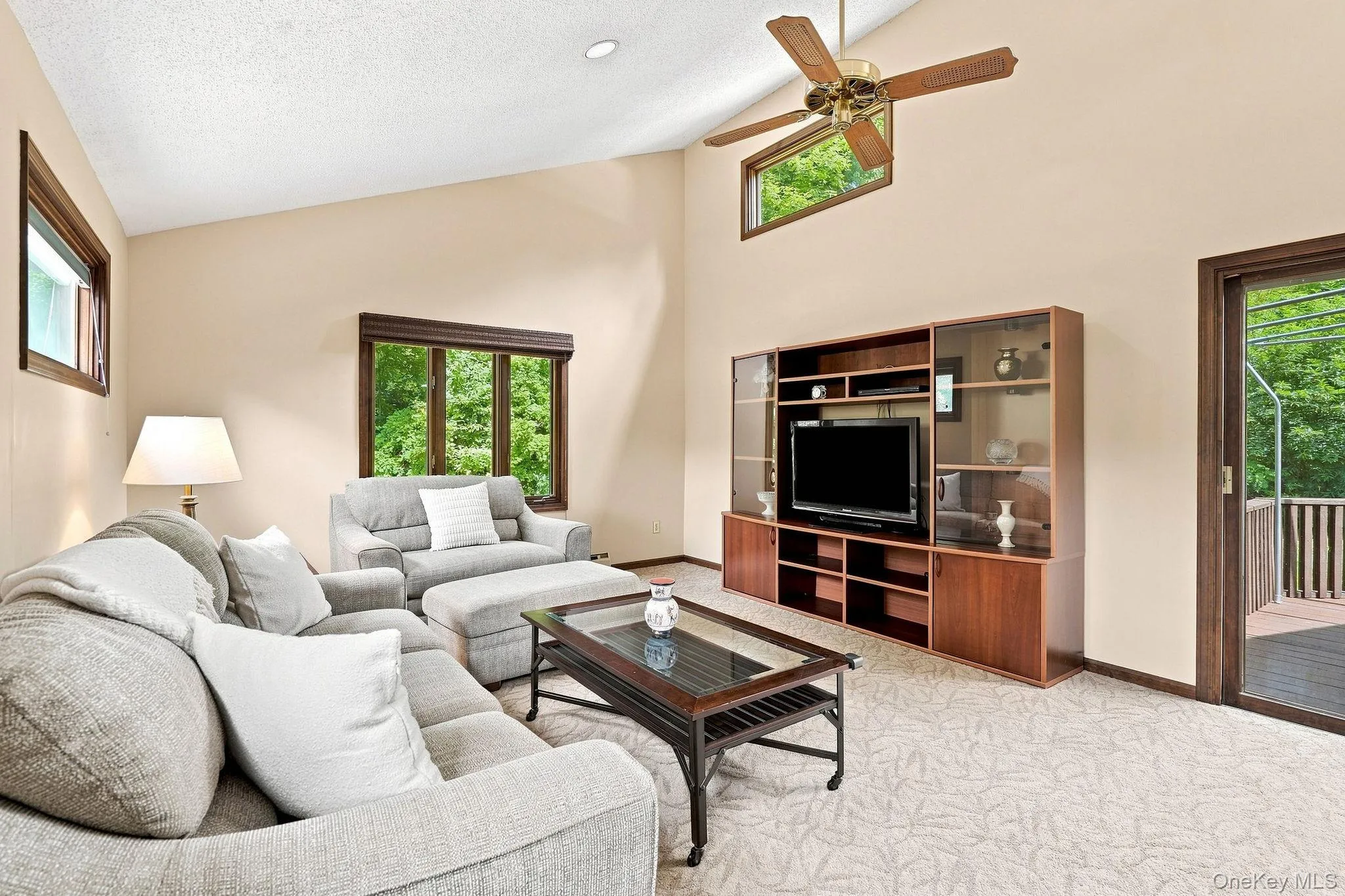 Vaulted ceiling with a ceiling fan, multiple windows, wood-finish built-in media center, and light-toned carpet Vaulted ceiling with a ceiling fan, multiple windows, wood-finish built-in media center, and light-toned carpet