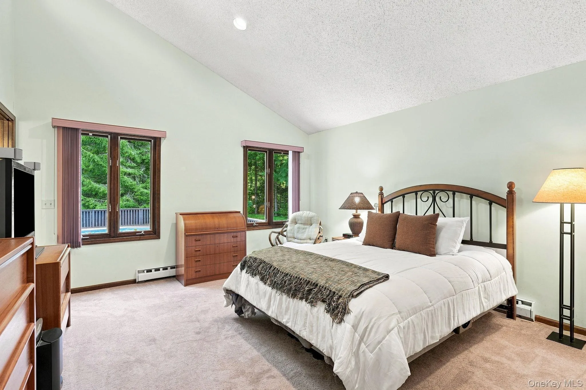 Vaulted ceiling primary bedroom with two large windows, wood-trim windows, and carpet flooring Vaulted ceiling primary bedroom with two large windows, wood-trim windows, and carpet flooring
