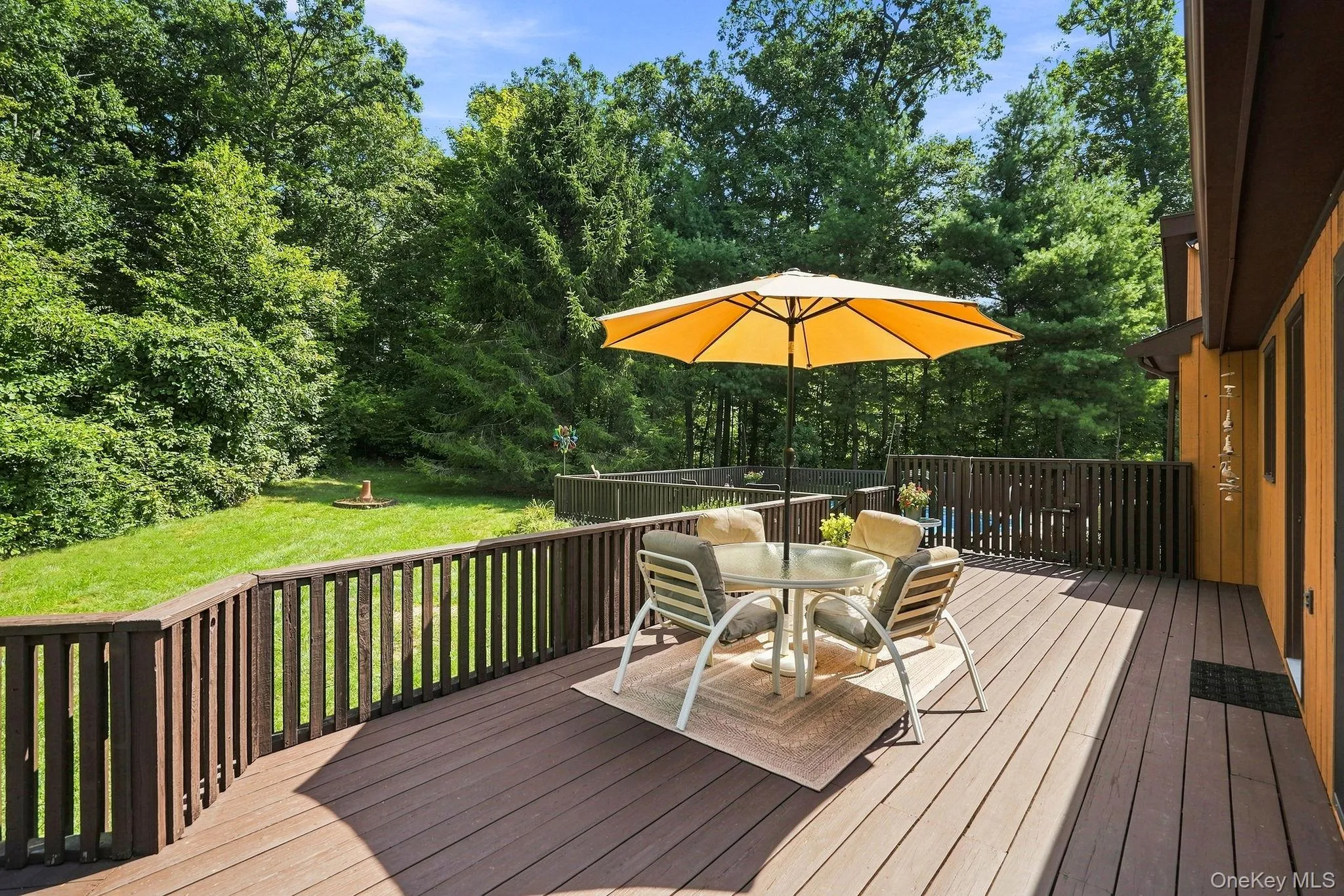 Expansive wood-finish deck with a wood railing overlooking a lush green lawn and mature trees Expansive wood-finish deck with a wood railing overlooking a lush green lawn and mature trees