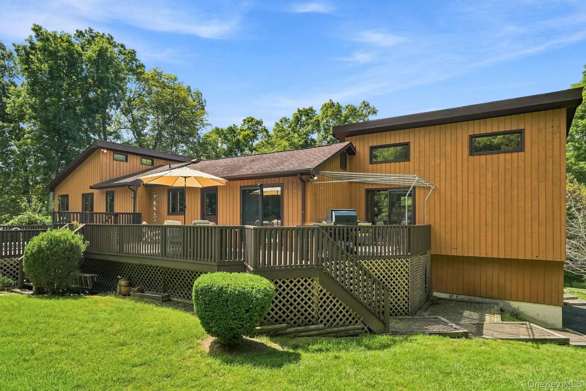 Rear exterior with wood siding, expansive wood deck, lattice skirting, and a sloping roofline Rear exterior with wood siding, expansive wood deck, lattice skirting, and a sloping roofline