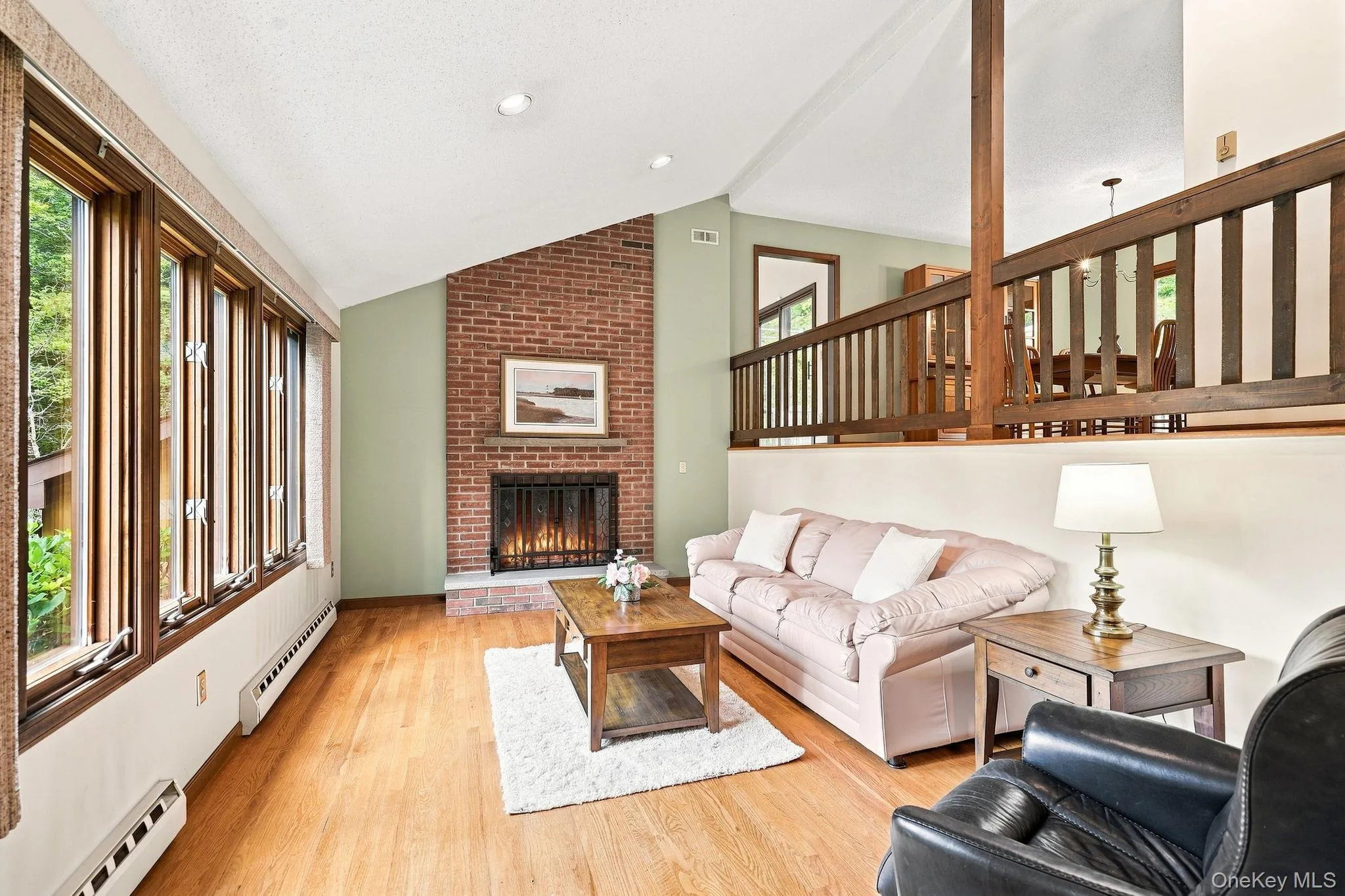 Vaulted ceiling with recessed lighting, brick fireplace with stone hearth, wood-frame windows, wood-finish flooring, and a wood railing overlooking the lower level Vaulted ceiling with recessed lighting, brick fireplace with stone hearth, wood-frame windows, wood-finish flooring, and a wood railing overlooking the lower level