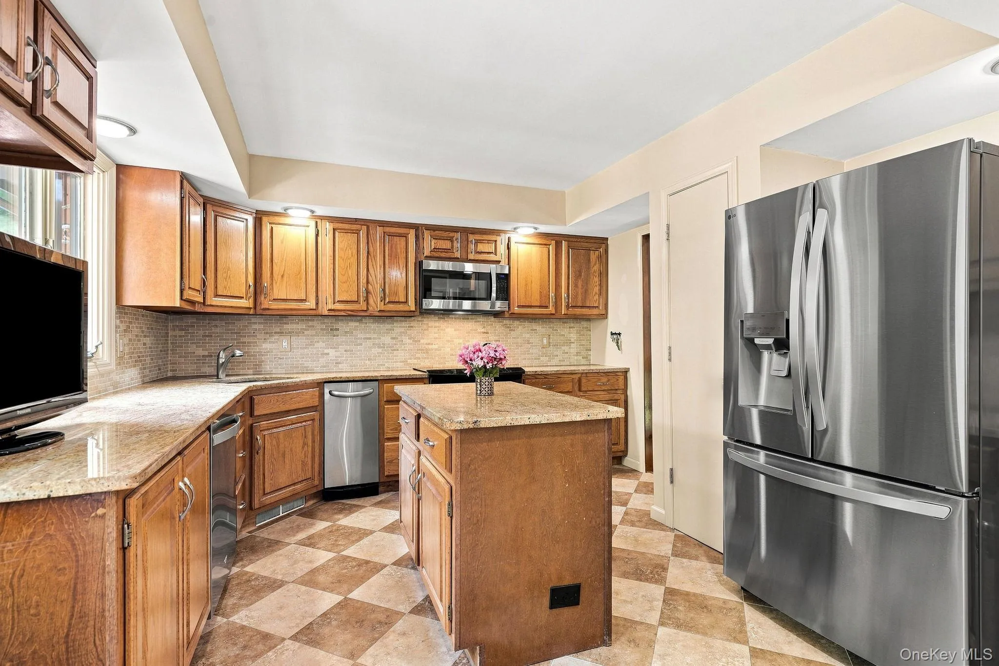 Kitchen featuring wood cabinetry, light-toned countertops, a mosaic tile backsplash, stainless steel appliances, and checkerboard floor tiling Kitchen featuring wood cabinetry, light-toned countertops, a mosaic tile backsplash, stainless steel appliances, and checkerboard floor tiling