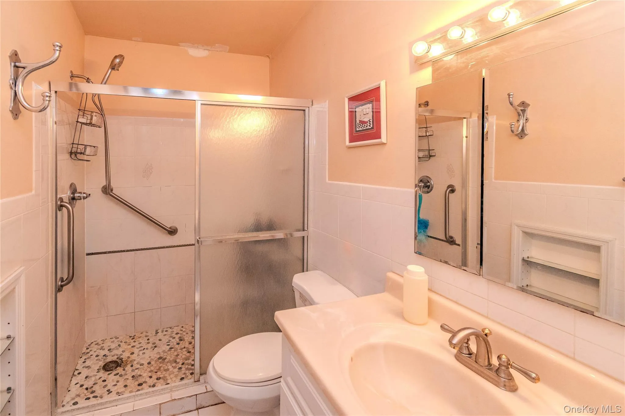 Walk-in shower with grab bars and a pebble-finish floor, adjacent to a vanity with a drop-in sink, and a medicine cabinet Walk-in shower with grab bars and a pebble-finish floor, adjacent to a vanity with a drop-in sink, and a medicine cabinet