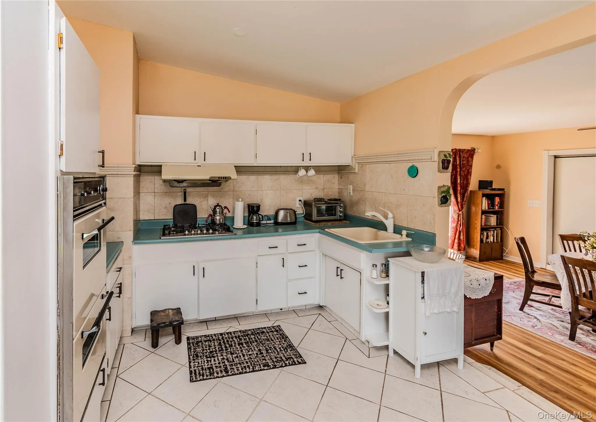 White cabinetry with matte black hardware, integrated wall oven, tile backsplash, light-colored countertops, and tile flooring White cabinetry with matte black hardware, integrated wall oven, tile backsplash, light-colored countertops, and tile flooring