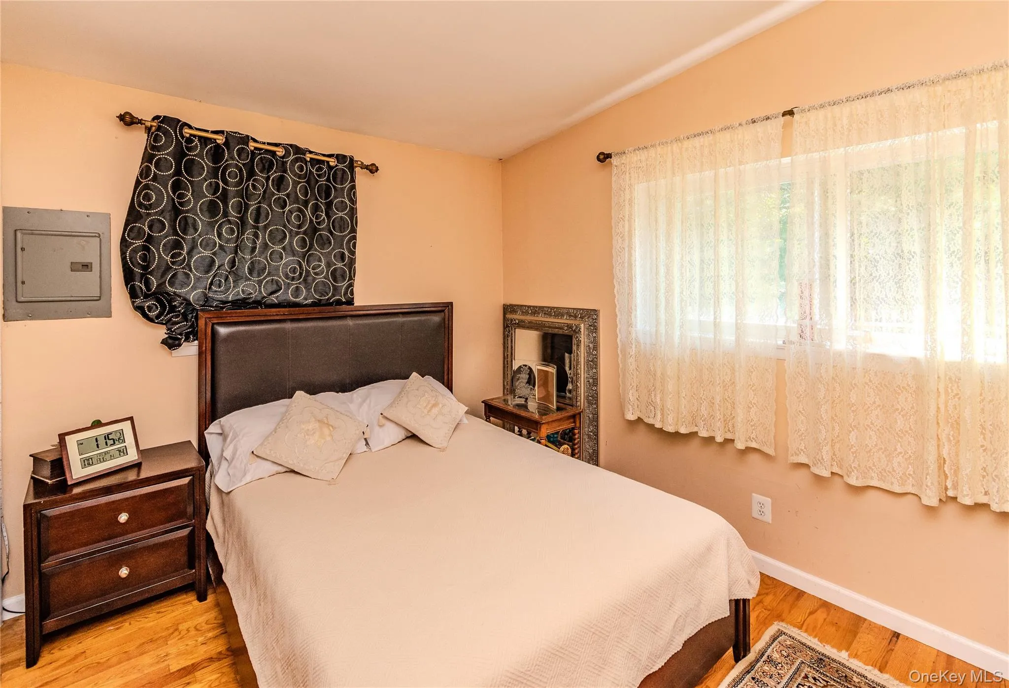 Warm, inviting bedroom featuring warm peach walls, wood-finish flooring, and abundant natural light from large windows dressed in sheer curtains Warm, inviting bedroom featuring warm peach walls, wood-finish flooring, and abundant natural light from large windows dressed in sheer curtains