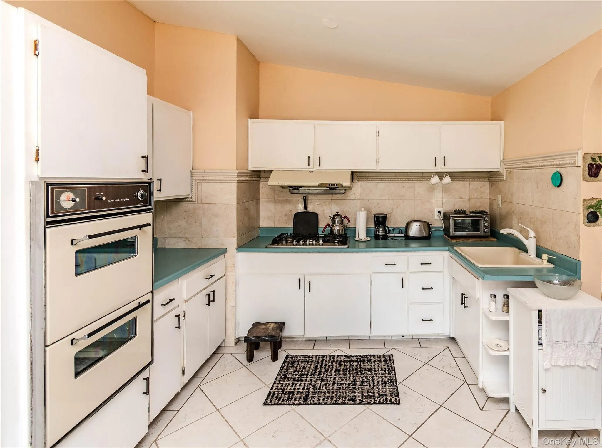 Kitchen featuring white cabinetry, a built-in double oven, a tiled backsplash, and light-colored floor tiles Kitchen featuring white cabinetry, a built-in double oven, a tiled backsplash, and light-colored floor tiles