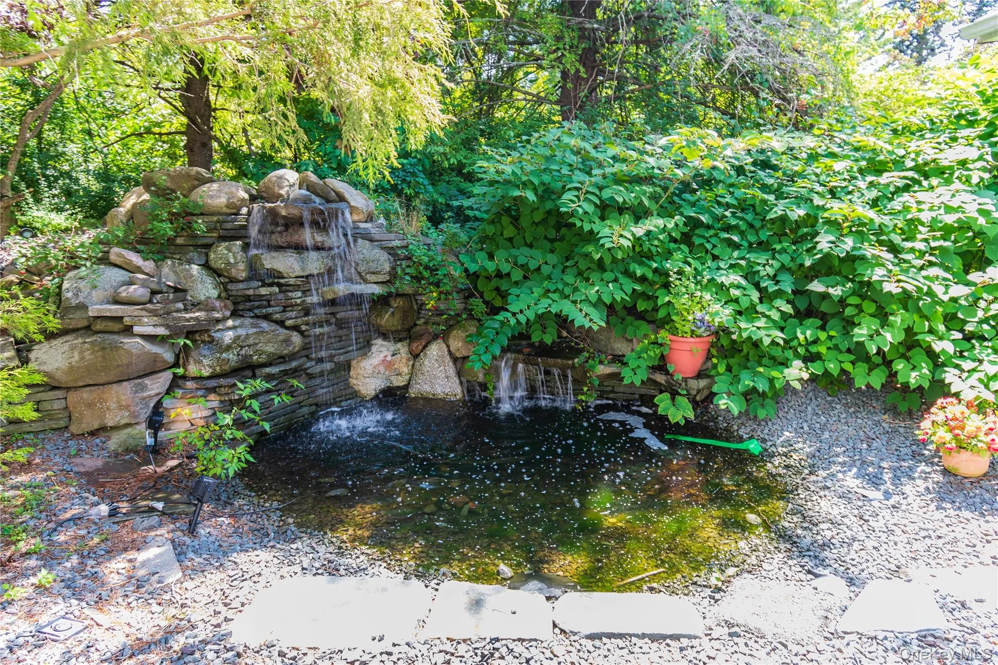 Stone waterfall feature, integrated pond, lush perimeter plantings, and natural stone step pavers Stone waterfall feature, integrated pond, lush perimeter plantings, and natural stone step pavers