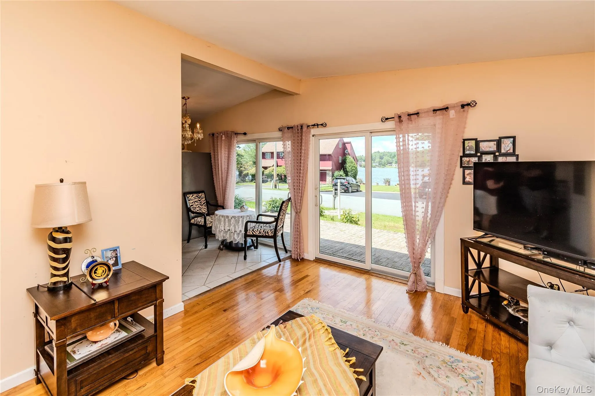 Warm, open living space featuring gleaming wood-finish flooring throughout, large glass sliding doors with sheer curtains, and abundant natural light Warm, open living space featuring gleaming wood-finish flooring throughout, large glass sliding doors with sheer curtains, and abundant natural light