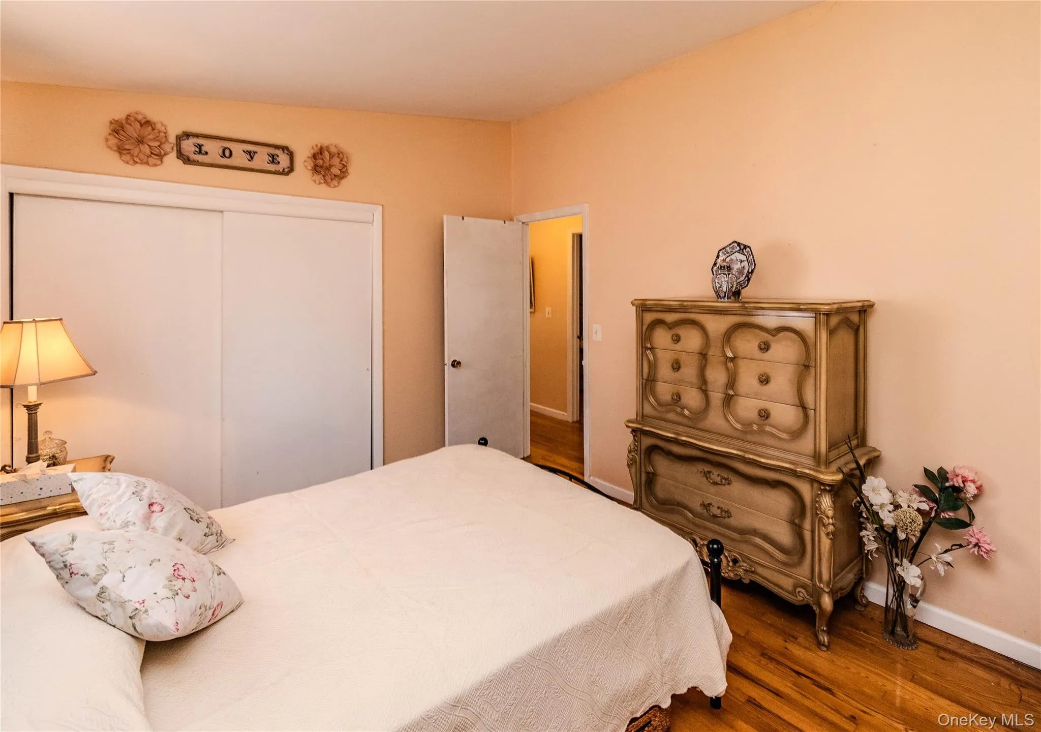 Serene primary bedroom featuring warm peachy-toned walls, hardwood flooring, and ample natural light Serene primary bedroom featuring warm peachy-toned walls, hardwood flooring, and ample natural light