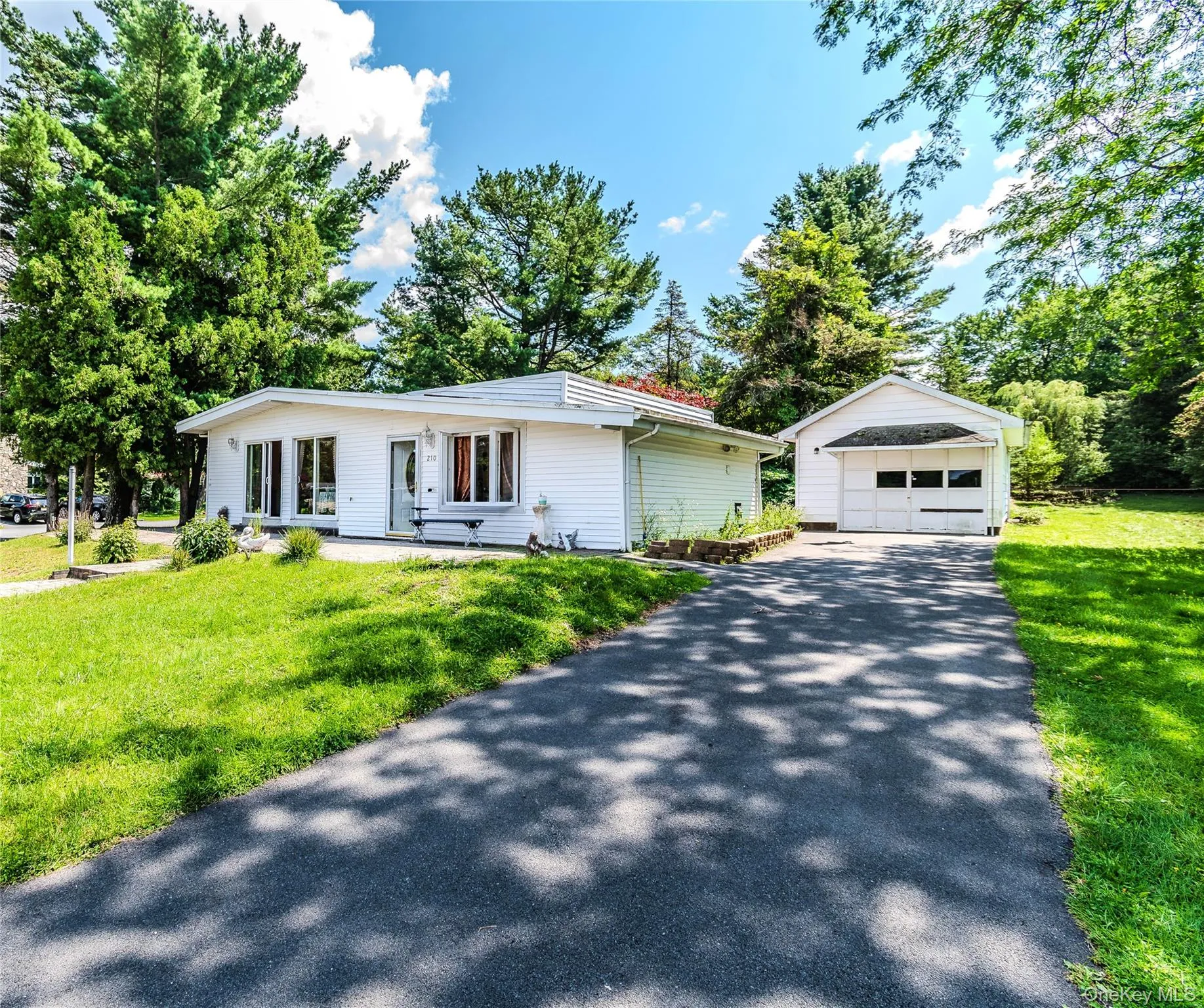 White siding exterior with multiple windows, a long paved driveway, detached garage, and mature trees White siding exterior with multiple windows, a long paved driveway, detached garage, and mature trees