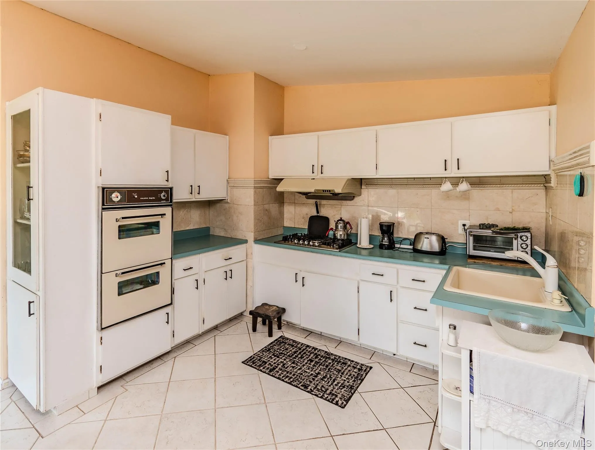 White cabinetry, dual built-in ovens, a gas cooktop, and tile flooring White cabinetry, dual built-in ovens, a gas cooktop, and tile flooring