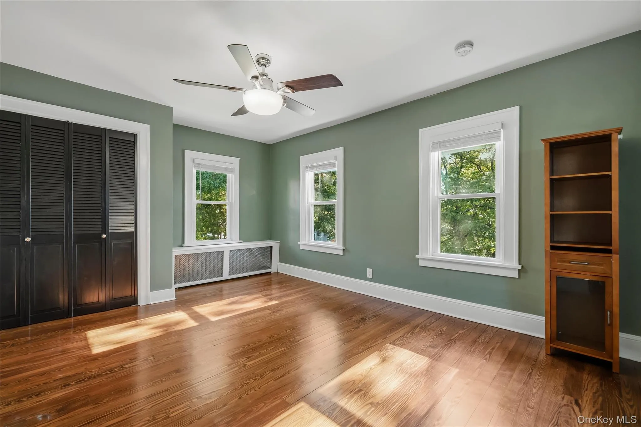 Hardwood flooring, painted walls, ceiling fan with integrated lighting, multiple windows, and a built-in radiator cover Hardwood flooring, painted walls, ceiling fan with integrated lighting, multiple windows, and a built-in radiator cover