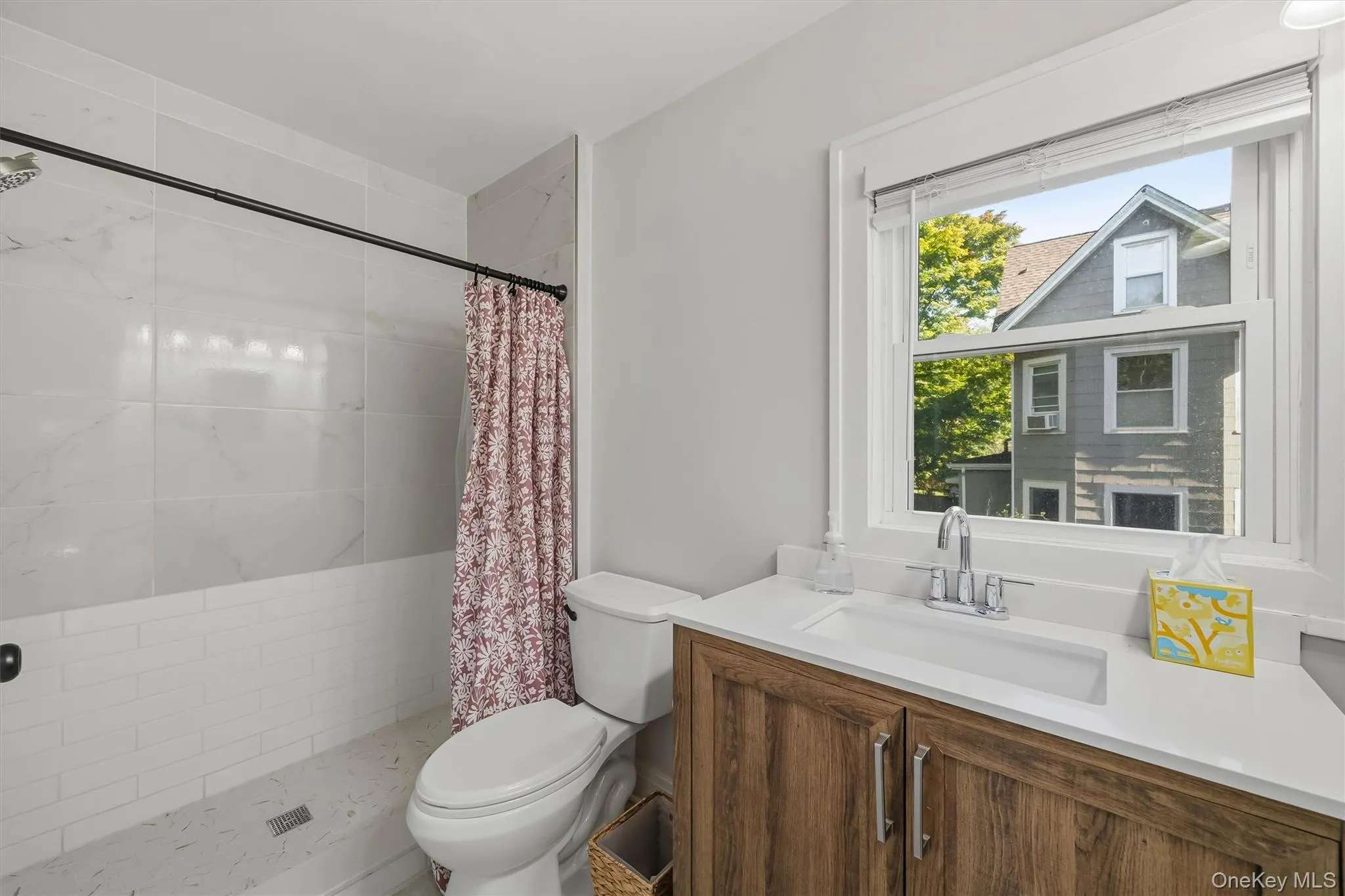 Bathroom featuring a wood-finish vanity, white quartz countertop, chrome faucet, and shower with subway tile surround Bathroom featuring a wood-finish vanity, white quartz countertop, chrome faucet, and shower with subway tile surround
