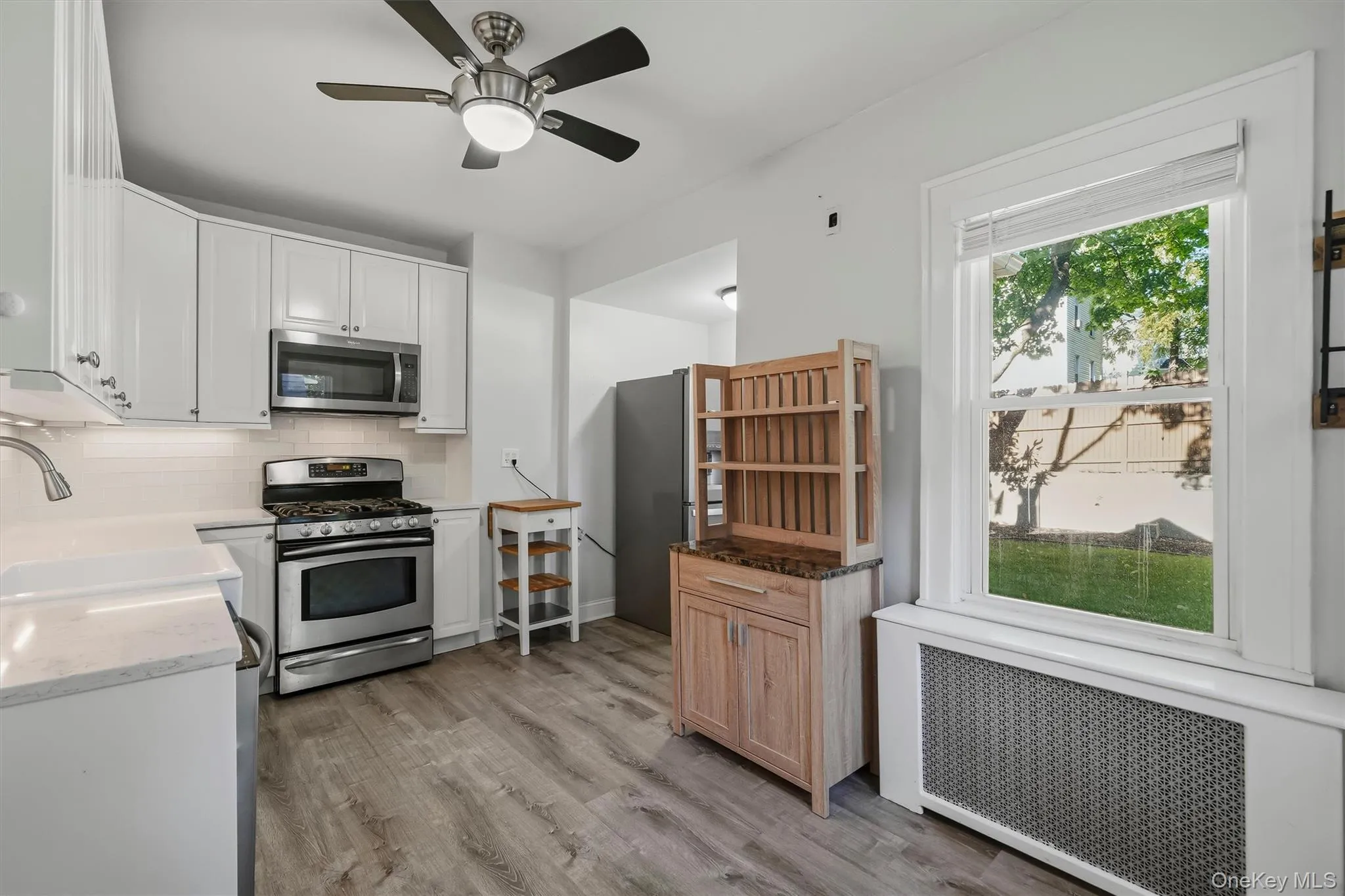 White shaker cabinetry, stainless steel appliances, wood-finish flooring, undermount sink, and recessed lighting with ceiling fan White shaker cabinetry, stainless steel appliances, wood-finish flooring, undermount sink, and recessed lighting with ceiling fan
