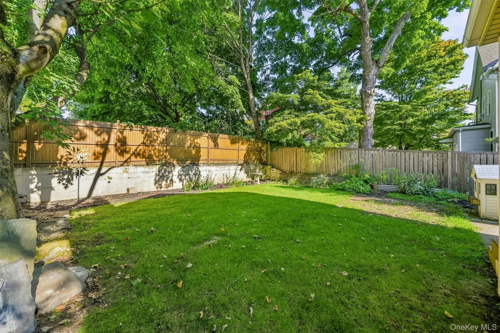 Lawn area with a perimeter wood fence, mature trees, and a concrete retaining wall Lawn area with a perimeter wood fence, mature trees, and a concrete retaining wall