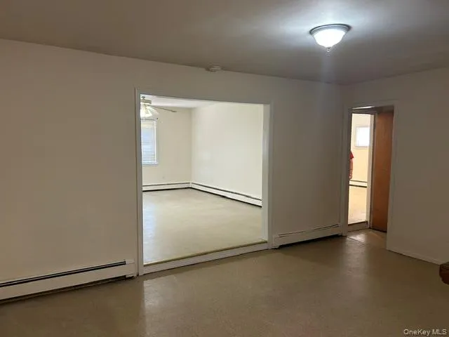 Recessed wall opening into family room, neutral wall paint, ceiling-mounted light fixture, and baseboard heating Recessed wall opening into family room, neutral wall paint, ceiling-mounted light fixture, and baseboard heating