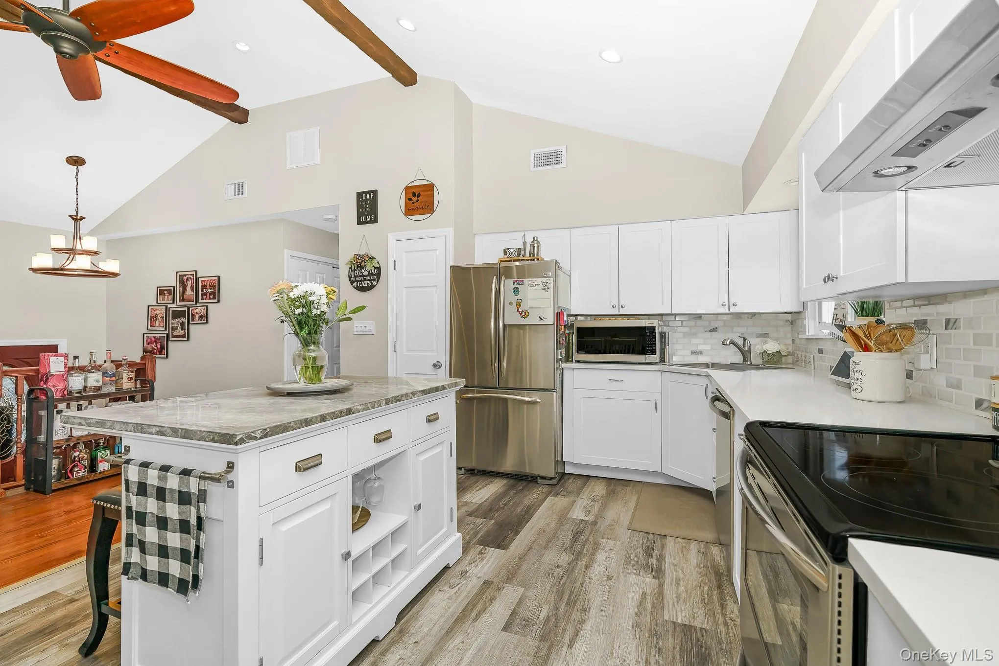 Kitchen featuring vaulted ceilings, wood-finish flooring, white cabinetry, a kitchen island with storage, and stainless steel appliances Kitchen featuring vaulted ceilings, wood-finish flooring, white cabinetry, a kitchen island with storage, and stainless steel appliances