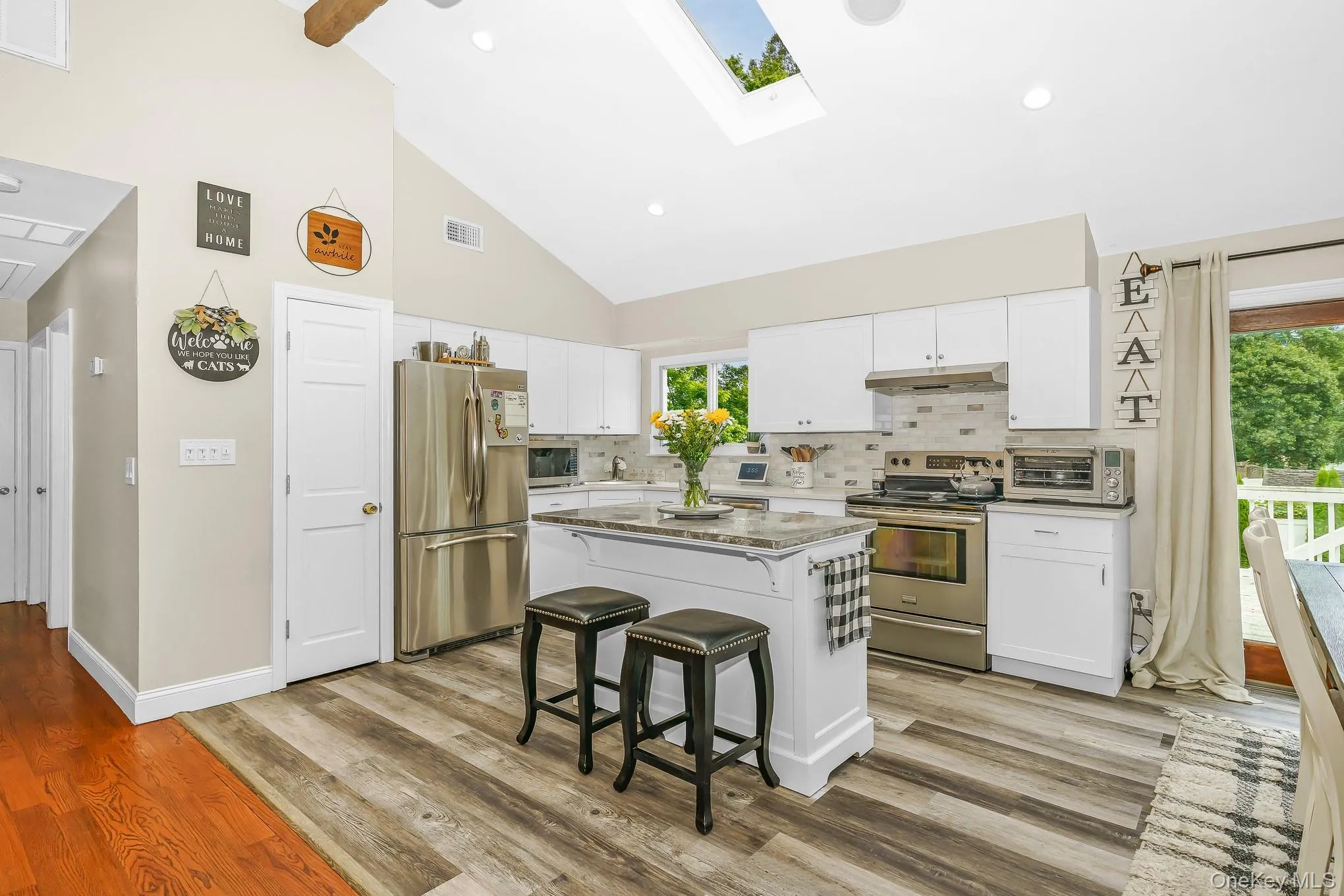 Vaulted ceiling with exposed wood beam, kitchen island with built-in storage, stainless steel appliances, skylight, and wood-finish flooring Vaulted ceiling with exposed wood beam, kitchen island with built-in storage, stainless steel appliances, skylight, and wood-finish flooring