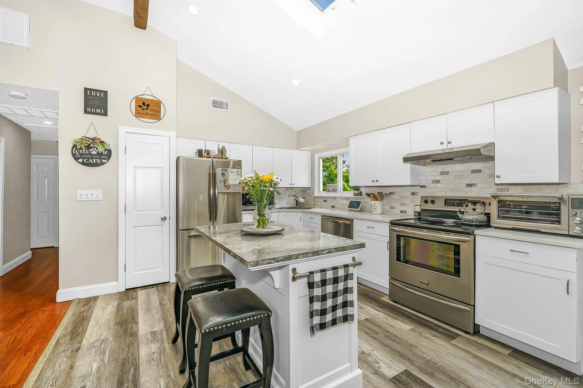 Vaulted ceiling, white shaker cabinetry, stainless steel appliances, central island with seating, and wood-finish flooring Vaulted ceiling, white shaker cabinetry, stainless steel appliances, central island with seating, and wood-finish flooring