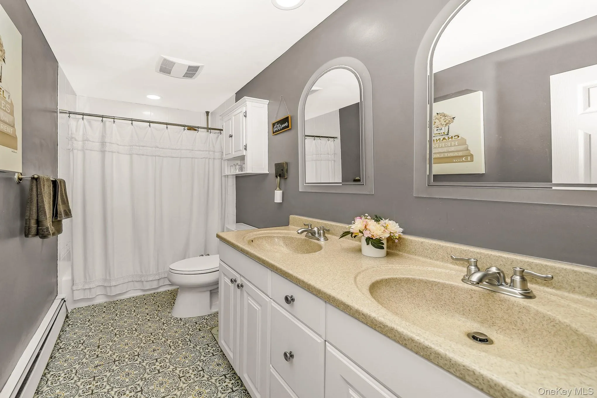 Double vanity with integrated sinks, arched mirrors, patterned floor tile, white shaker cabinetry, and a built-in shower/tub combination Double vanity with integrated sinks, arched mirrors, patterned floor tile, white shaker cabinetry, and a built-in shower/tub combination
